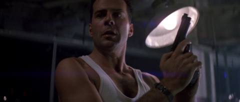 Bruce Willis, wearing a white tanktop and holding a pistol in Die Hard.