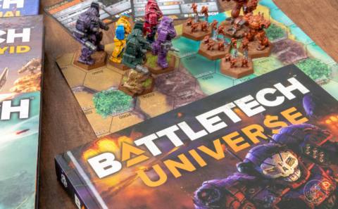 A photo of the Battletech Universe book alongside some tabletop maps and miniatures