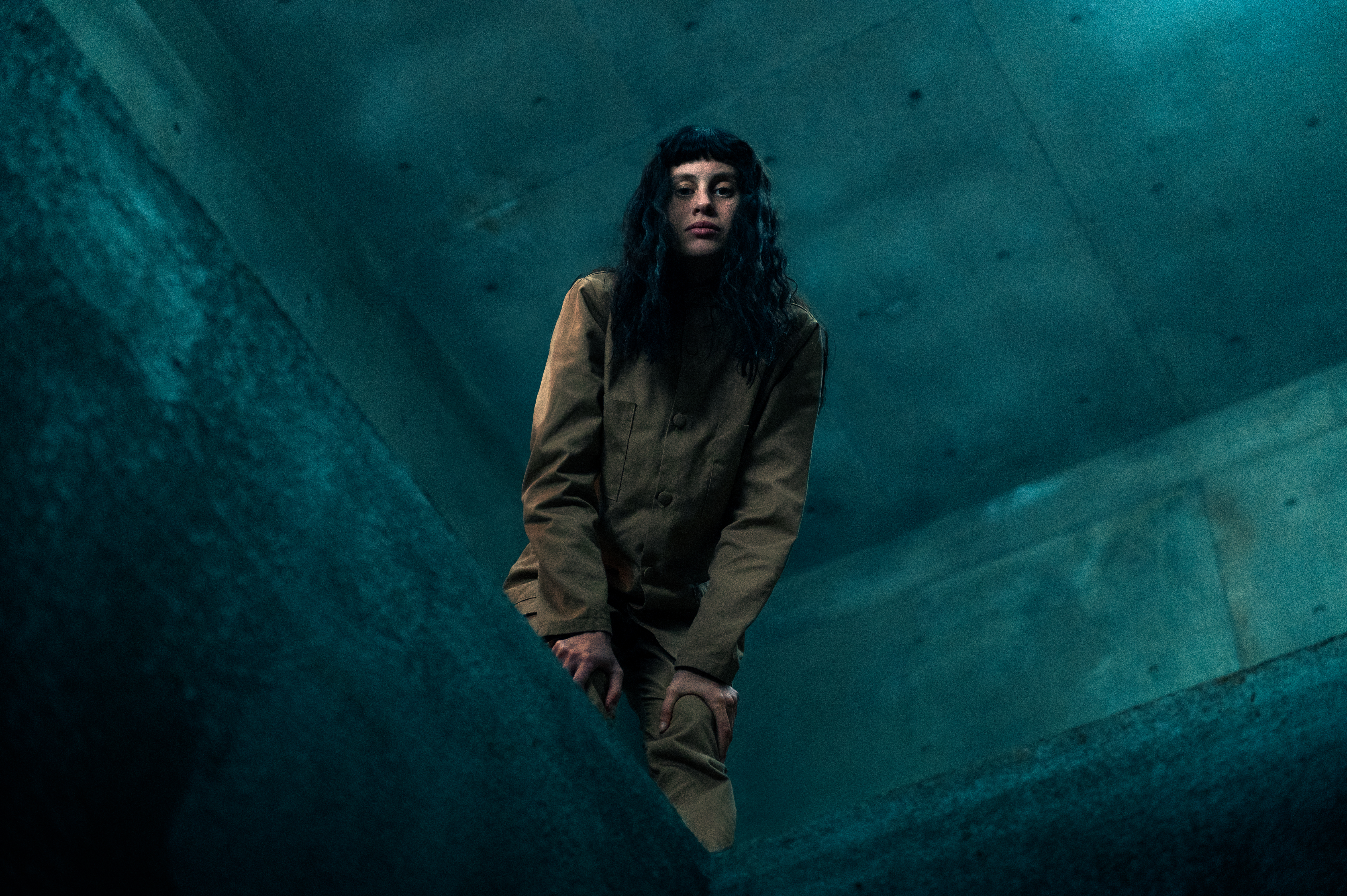 A woman in a tan jumpsuit leans over a ledge in The Platform 2.