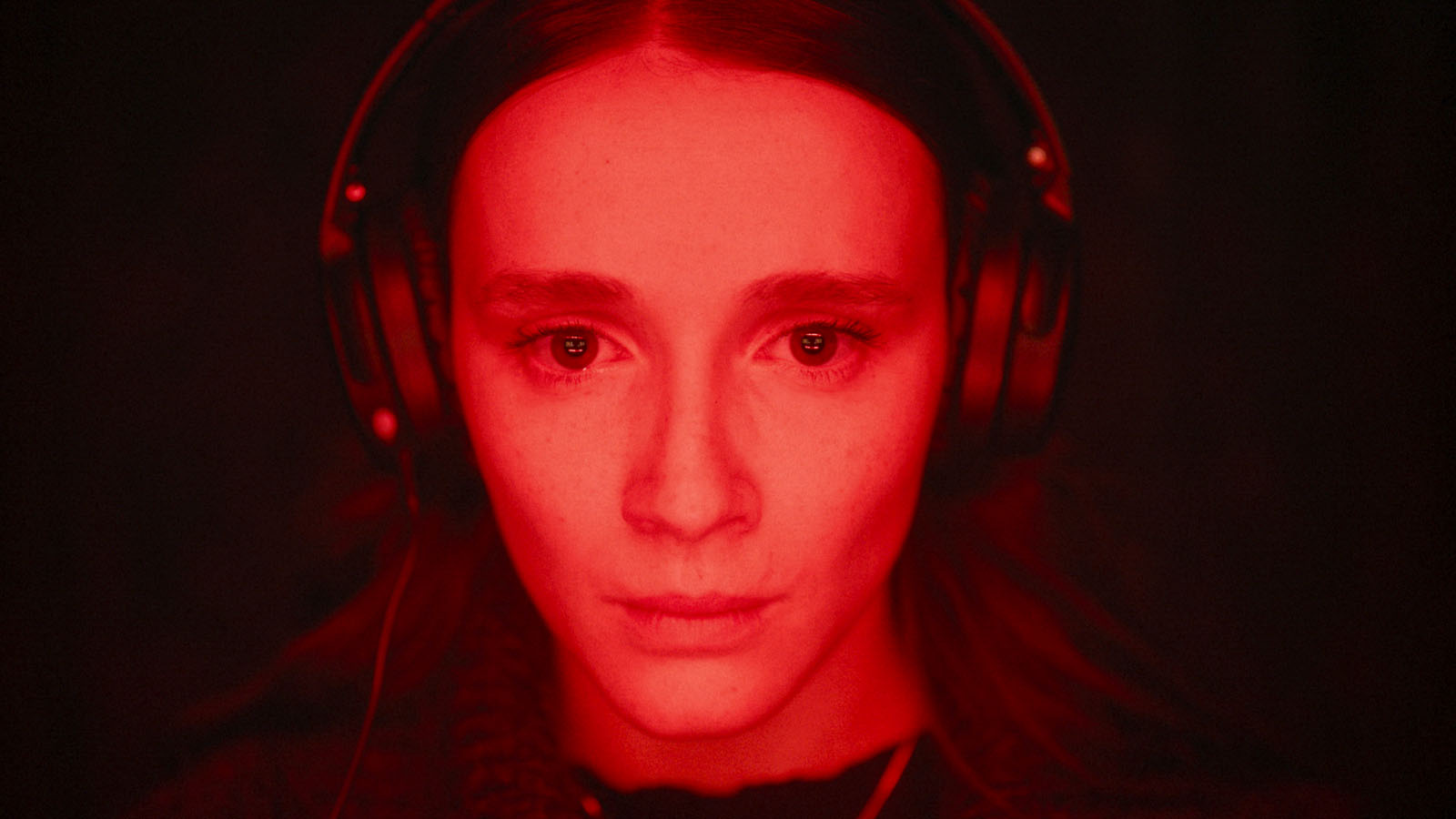 A woman wearing headphones bathed in an unearthly red glow in Red Rooms.