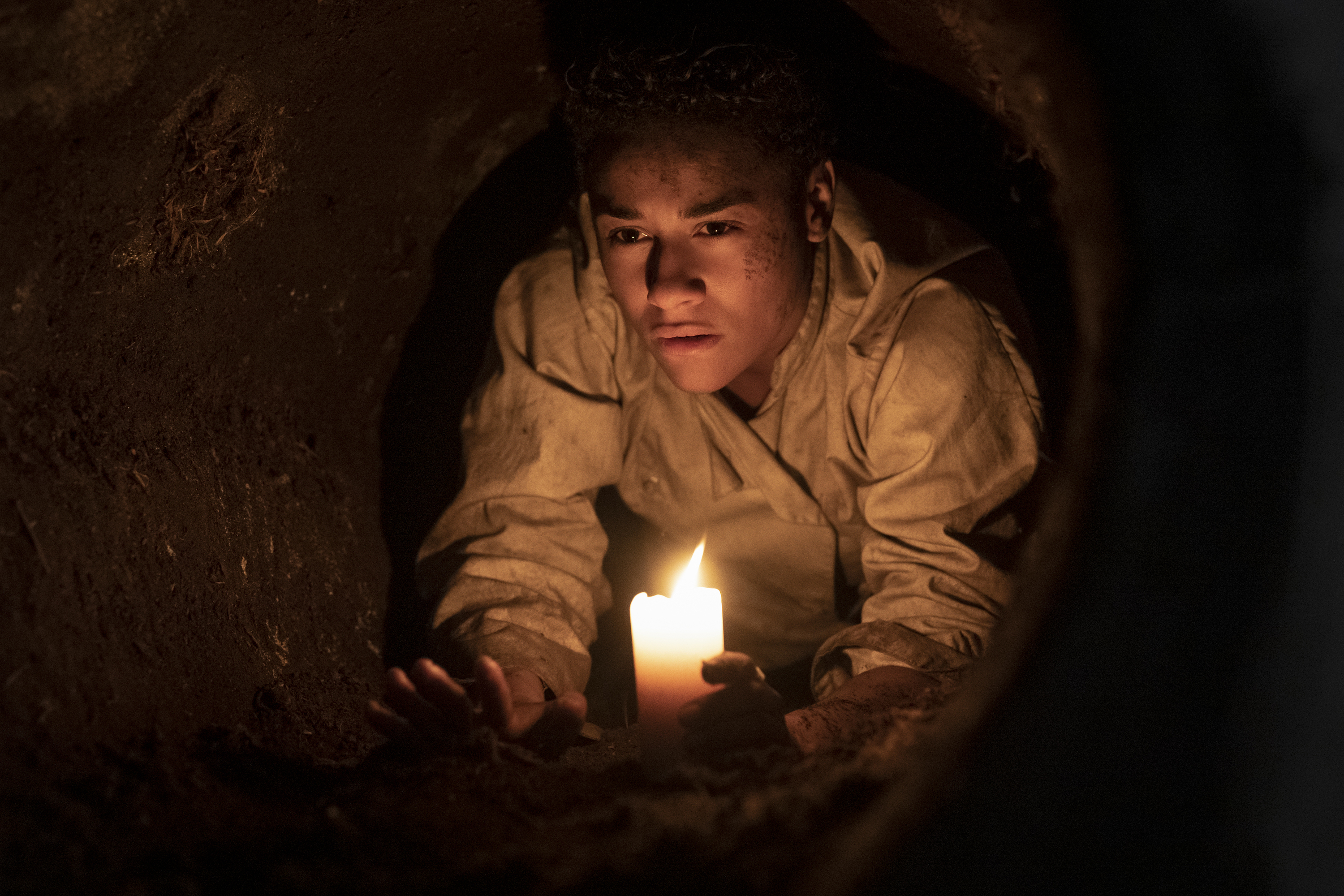 A woman in a chef’s uniform holding a candle in a cramped tunnel in House of Spoils.