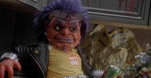 Orange-skinned, purple-haired, puppety-looking creature Frankie Freako lounging on a kitchen countertop drinking Fart soda in Frankie Freako