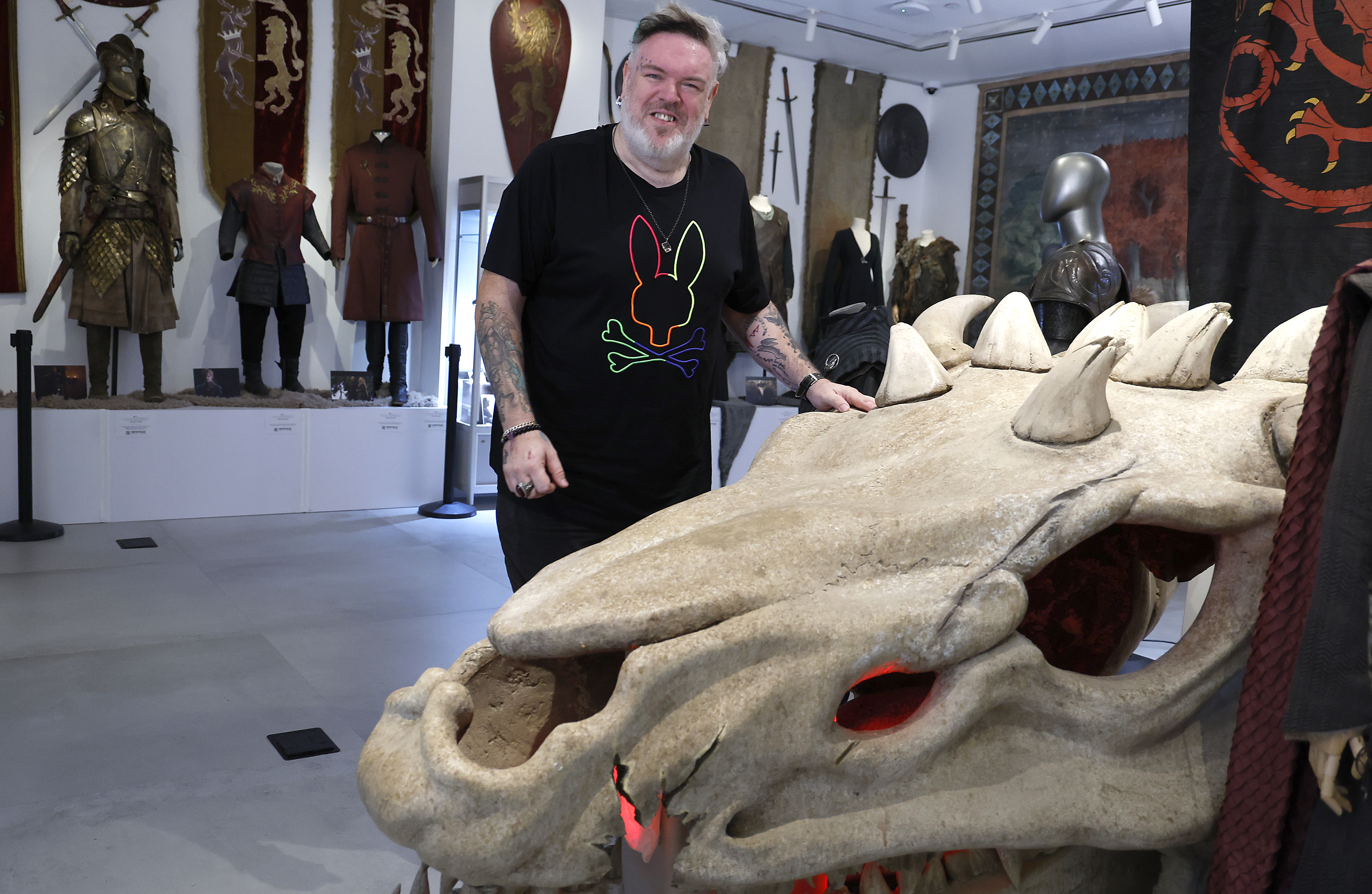 Game of Thrones and Our Flag Means Death actor Kristian Nairn stands smiling over an immense prop dragon skull at a Game of Thrones auction in New York City in 2024