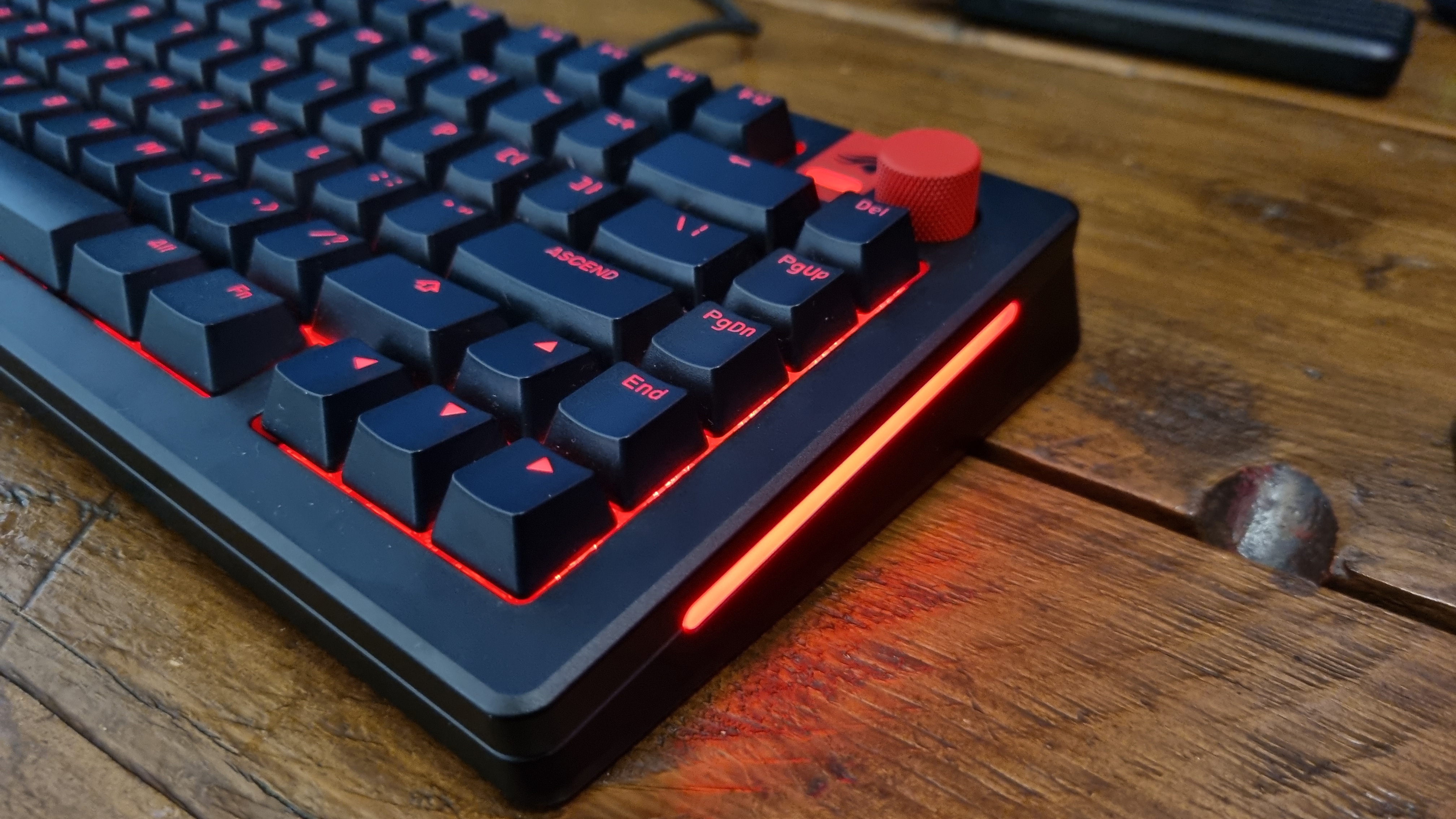 A side angle shot showing the sidelights of a fully customised Glorious GMMK 3 HE on a wooden desk, lit in red.