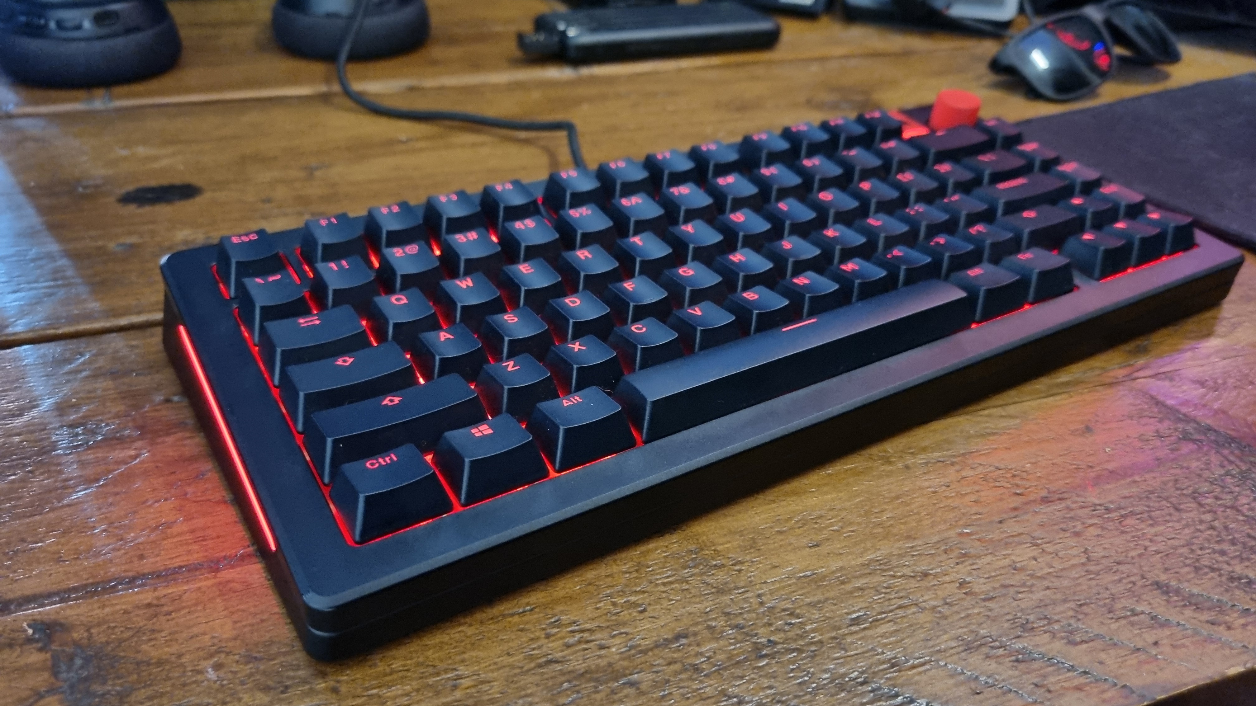 A fully customised Glorious GMMK 3 HE lit up in red on a wooden desk.