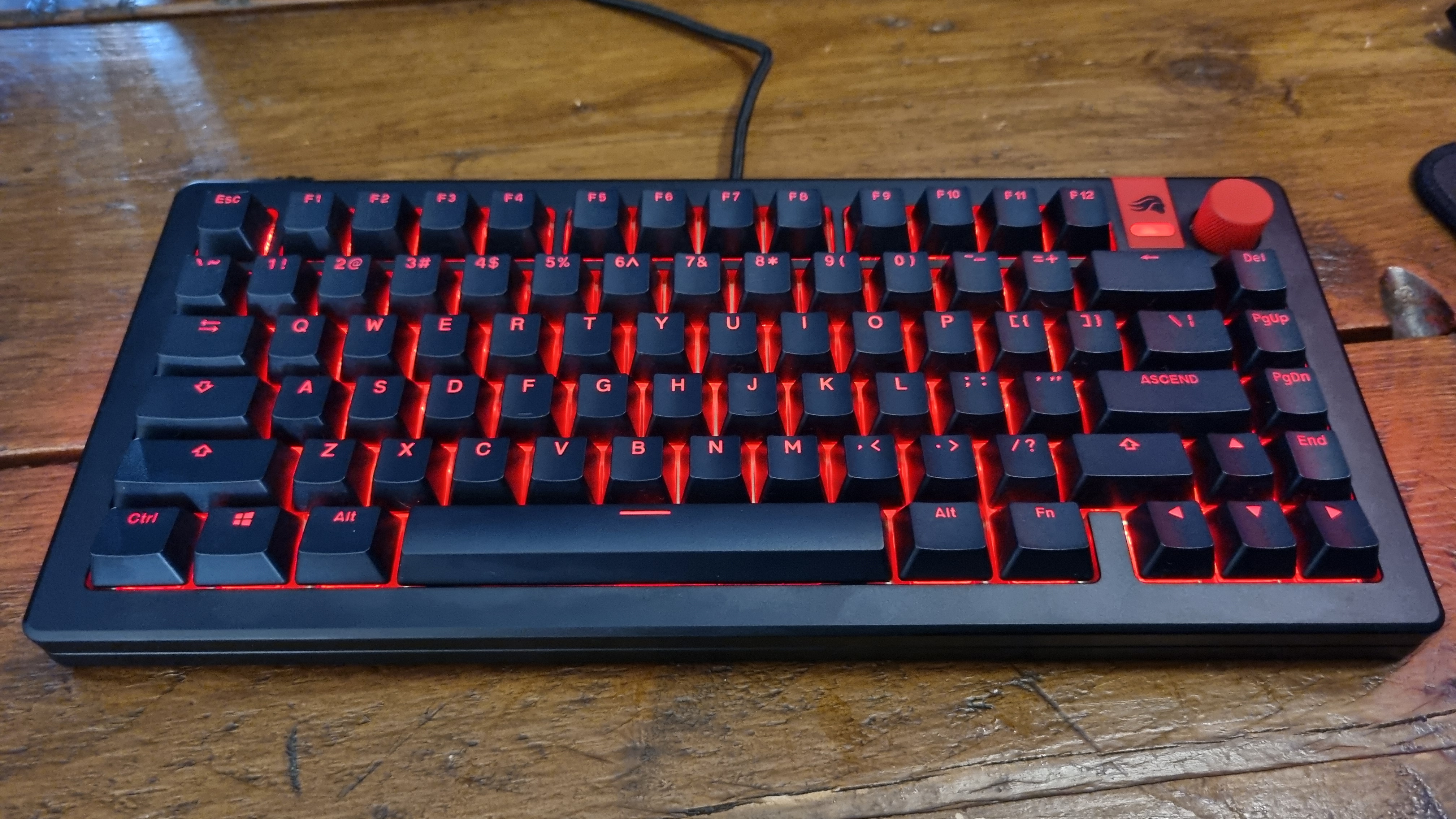 A shot of a fully customised GMMK 3 HE keyboard, glowing in red on a wooden desk.