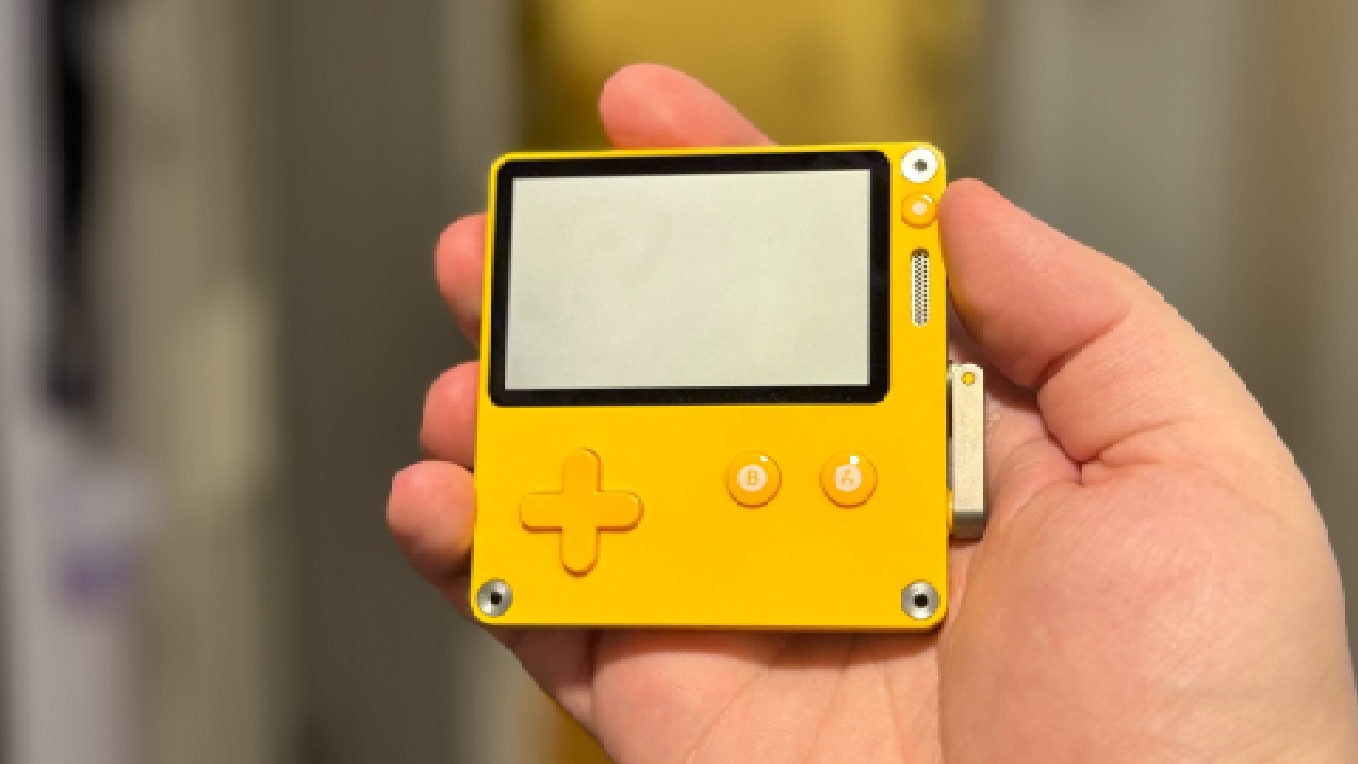 The Panic Playdate miniature gaming handheld, held, in this case, by a hand