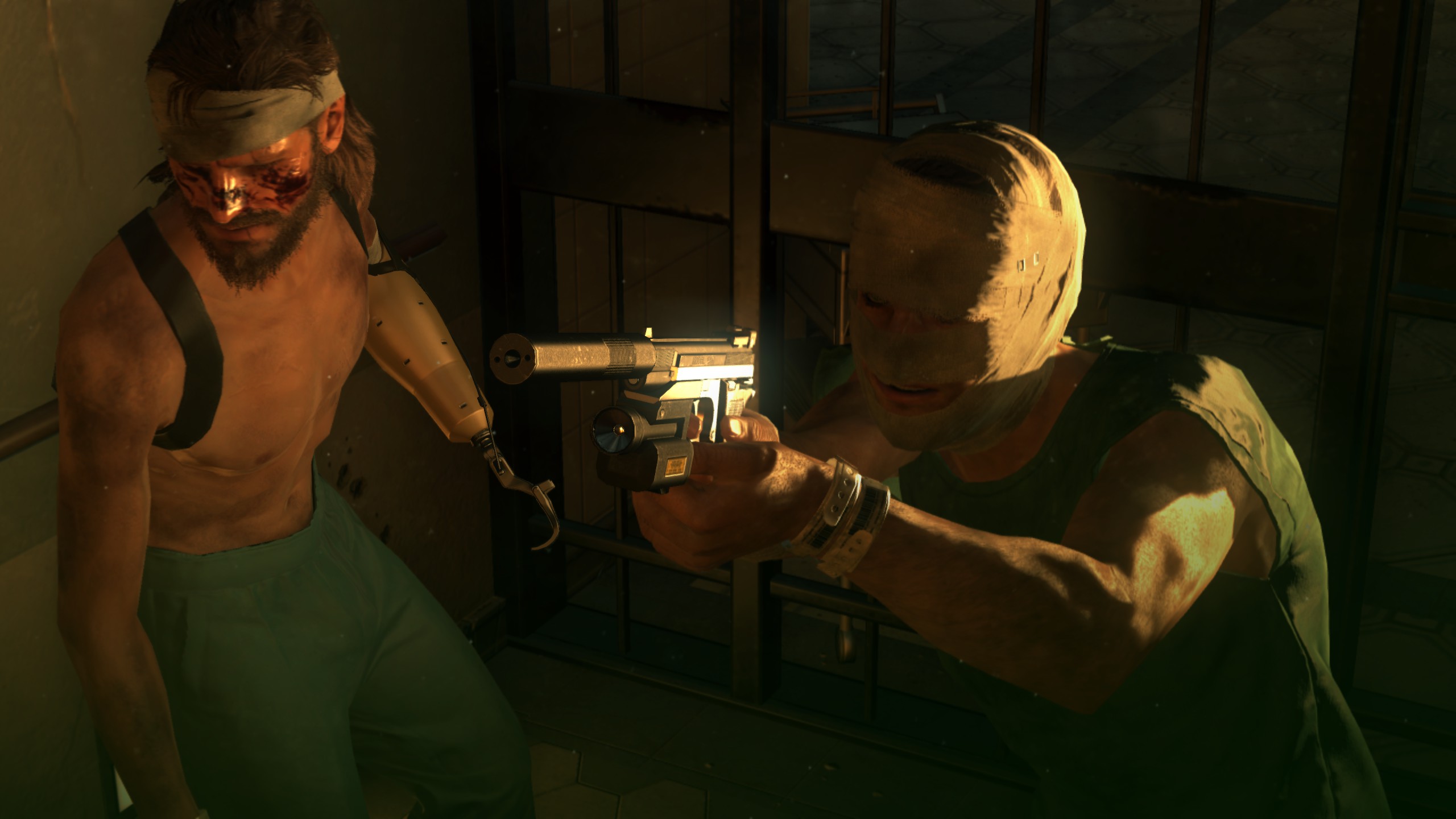 A shirtless man with a prosthetic arm standing next to a man with a bandaged face aiming a silenced pistol in Metal Gear Solid 5: The Phantom Pain.