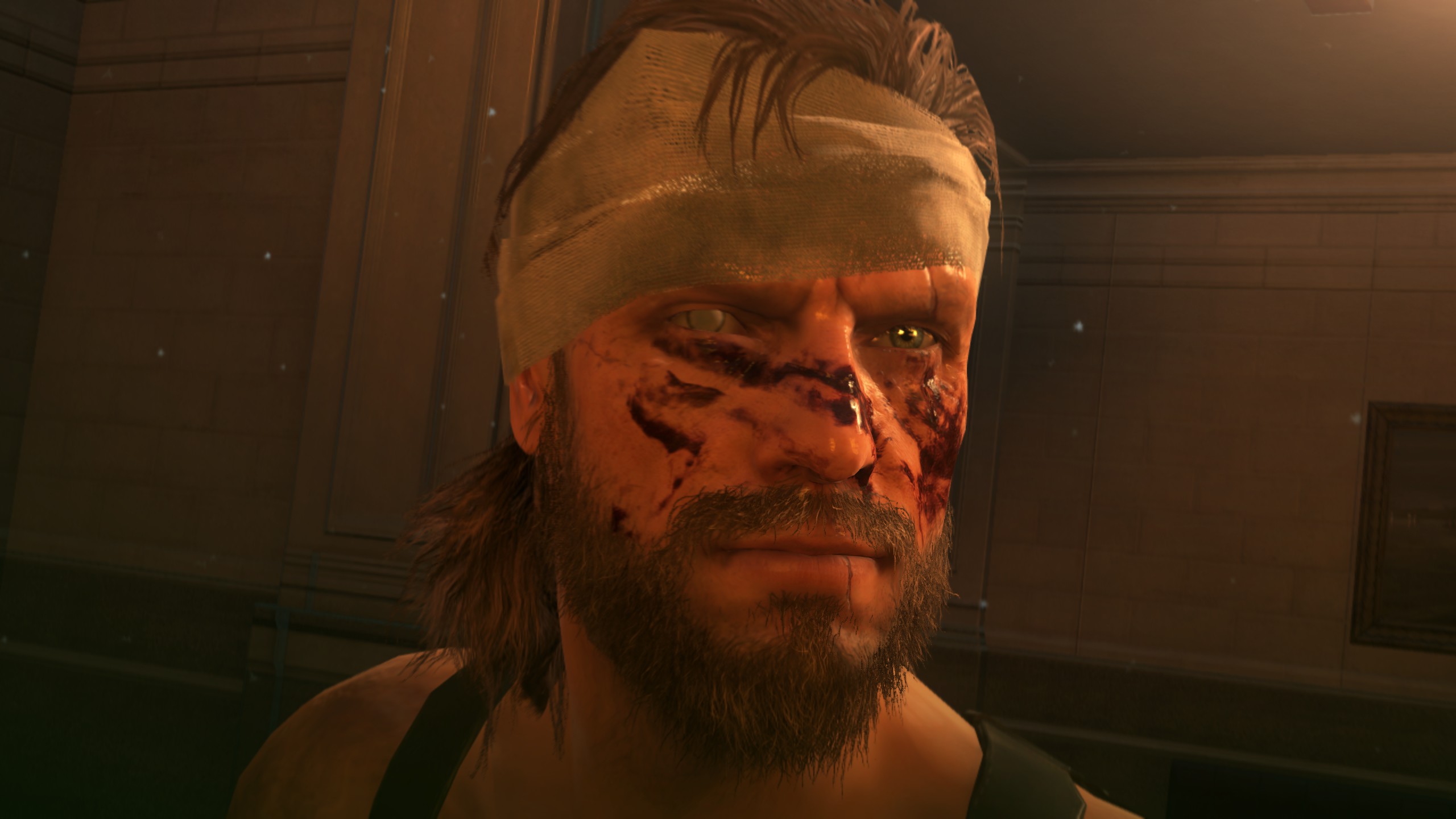 A close-up shot of a bearded man with bandages on his forehead, blood on his face, and a blinded eye in Metal Gear Solid 5: The Phantom Pain.