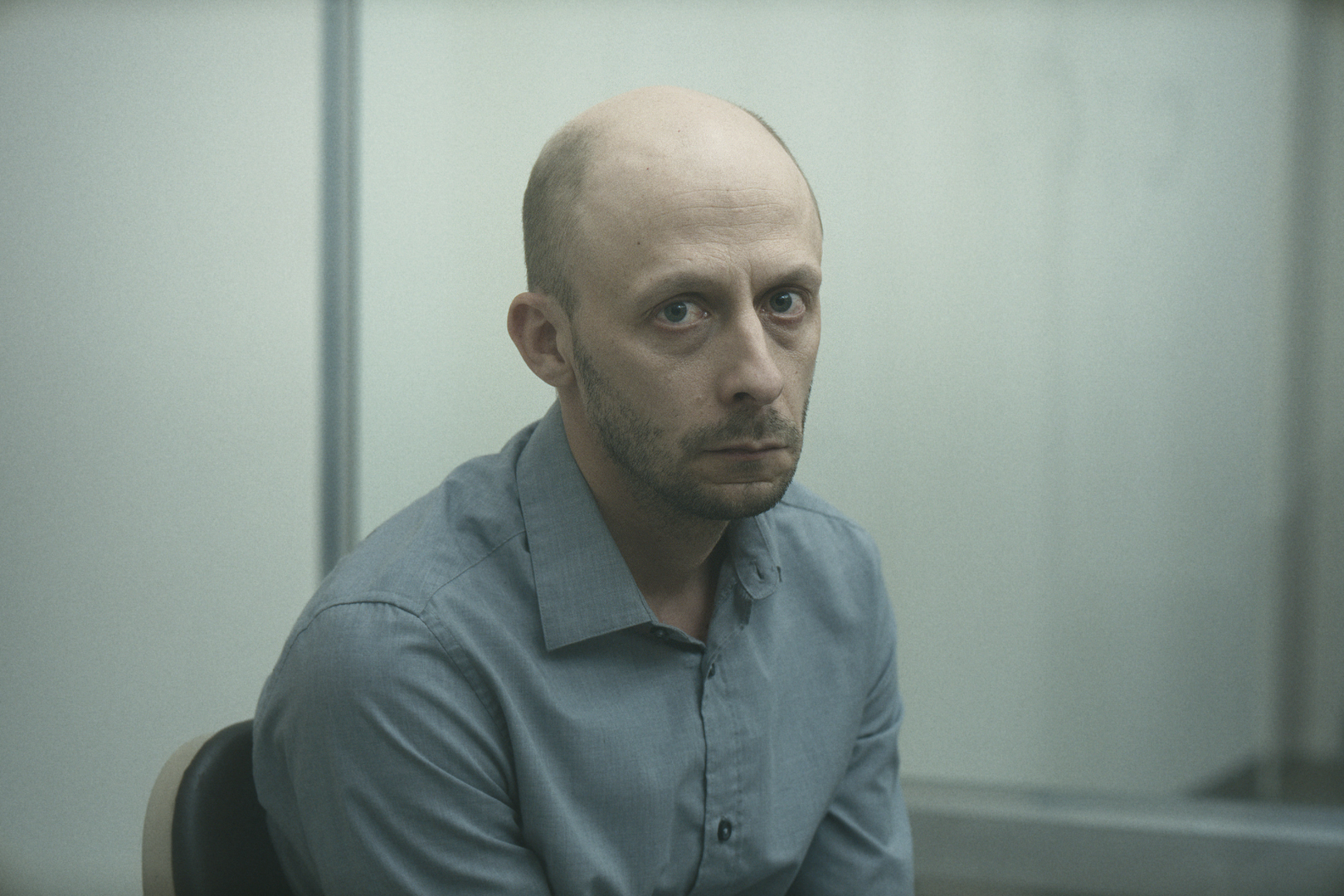 Chevalier, a bald man with a death stare, looks into the camera in Red Rooms 