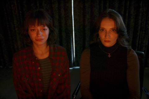 Two women stare at a computer screen, lit by the red glow, in Red Rooms