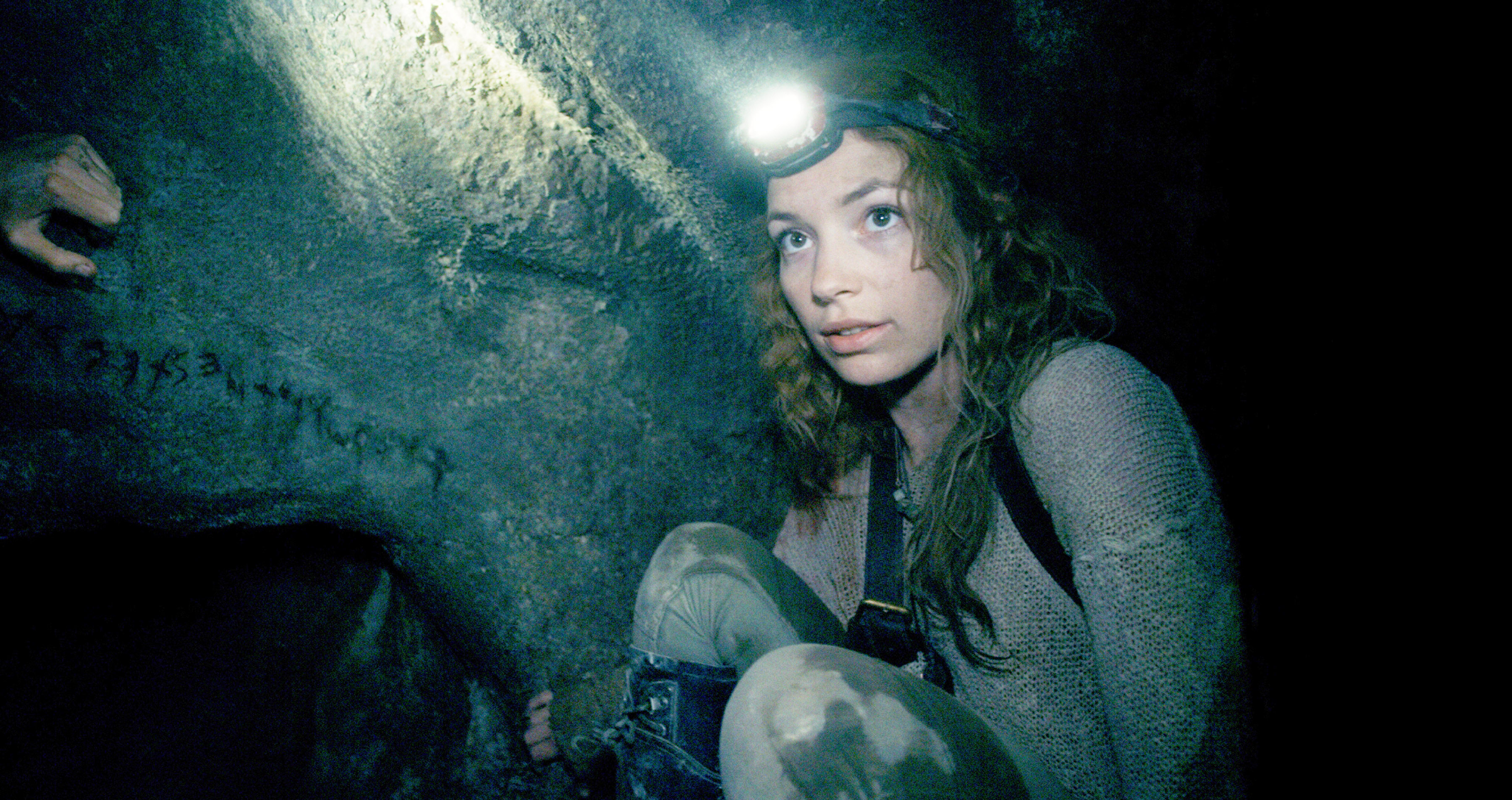 Perdita Weeks crouching in a cave wearing a headlamp in As Above, So Below