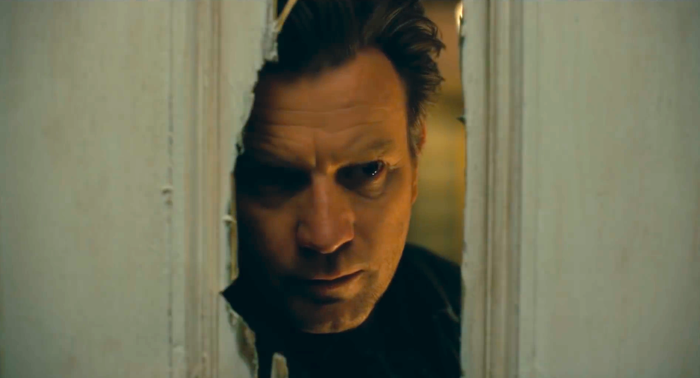 Ewan McGregor peering through a hole in a wooden door in Doctor Sleep.