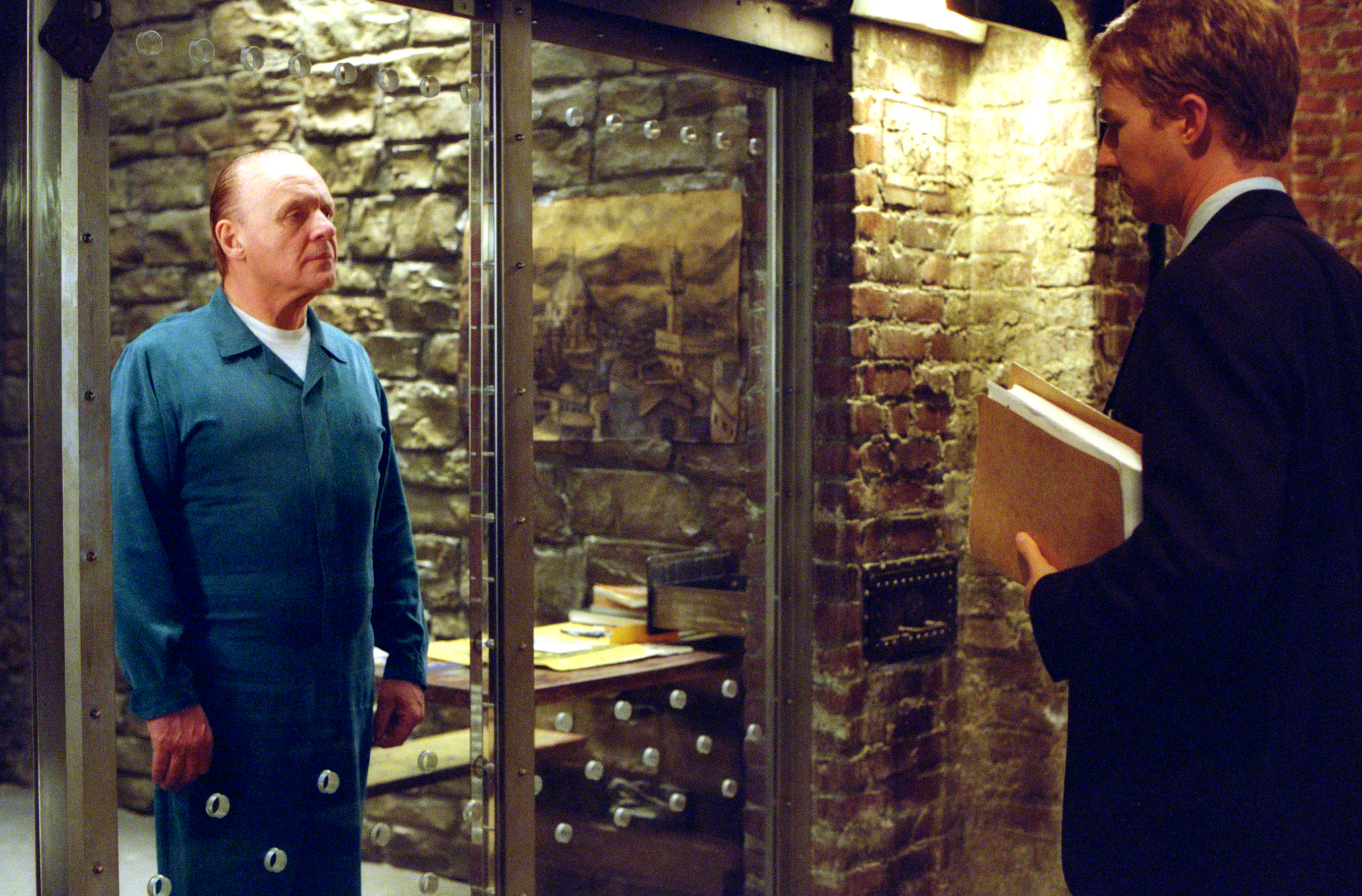 Anthony Hopkins as Doctor Hannibal Lecter and Edward Norton as Will Graham stand face to face in Red Dragon with Hopkins behind class in Hannibal Lecter’s iconic prison cell