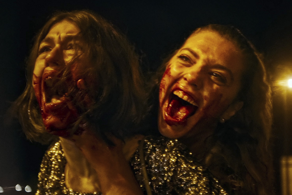 Two women with blood-splattered faces screaming in MADS.