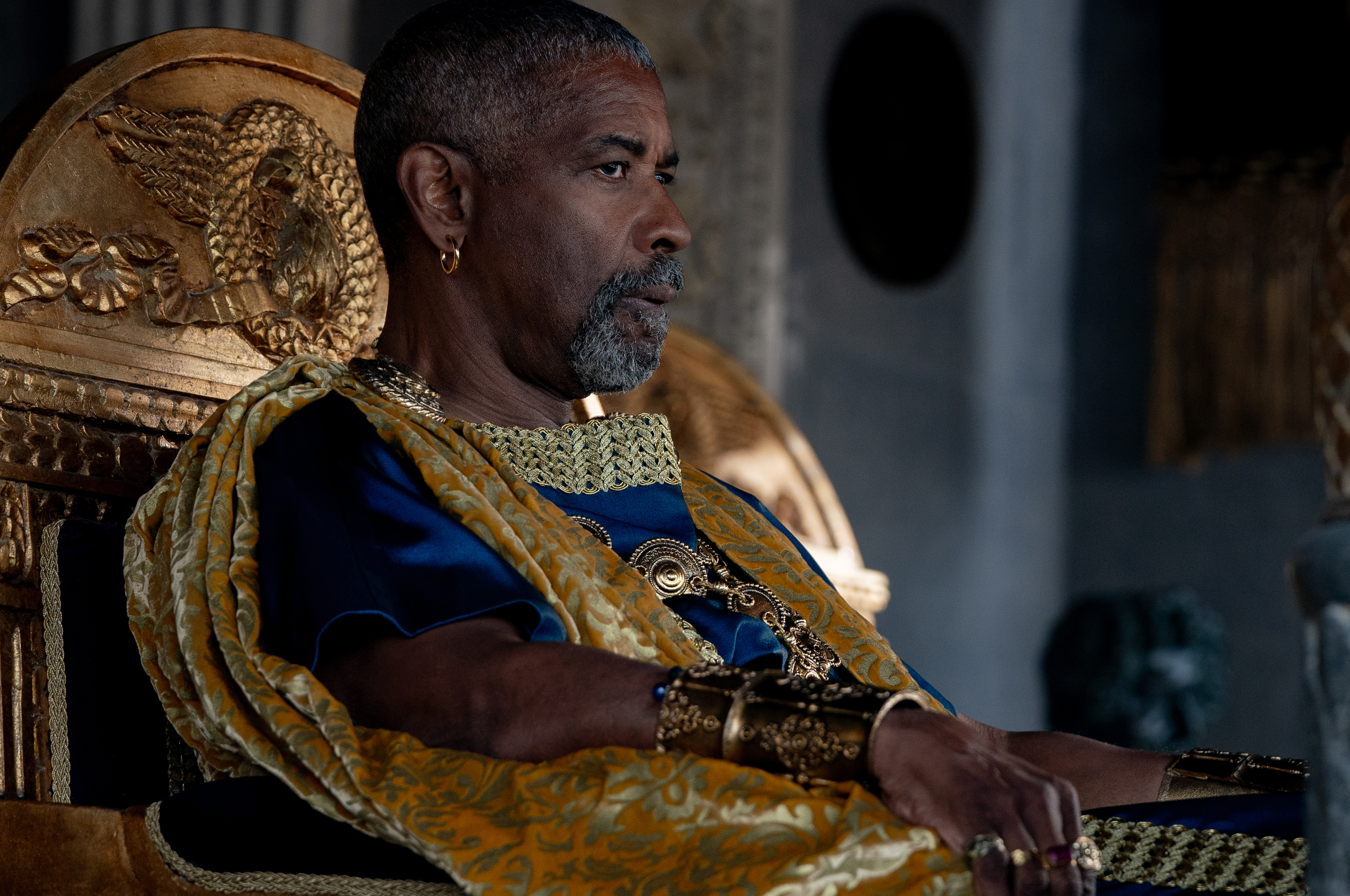 Denzel Washington looking worried while sitting on a gold throne in Gladiator 2