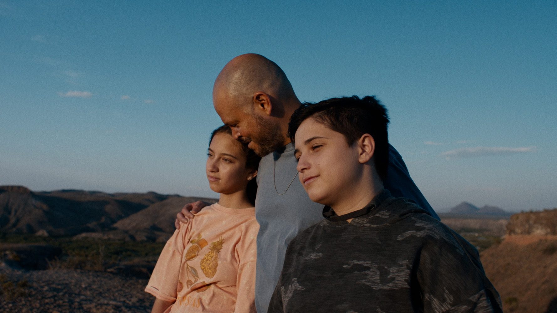 A man hugging his two children in In The Summers.