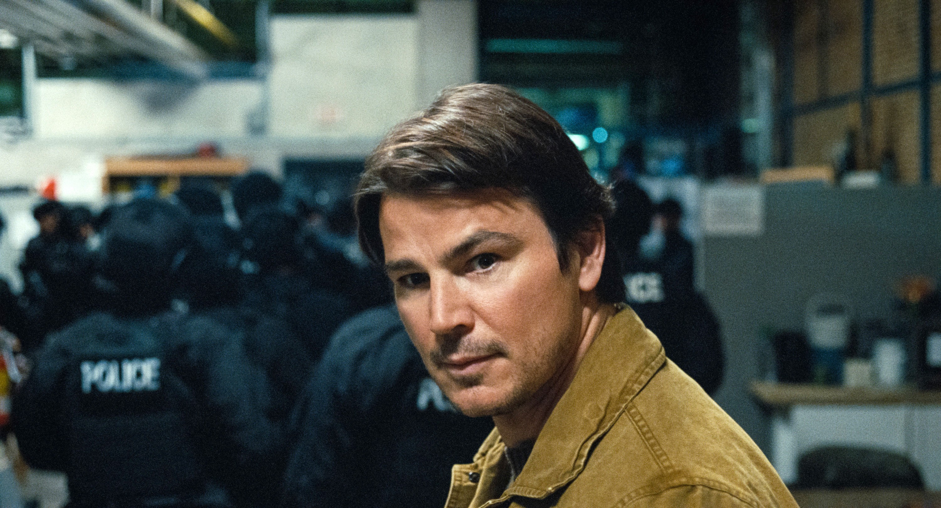Serial killer Cooper (Josh Hartnett) looks intently over his shoulder while approaching a group of armored police with their backs to him in M. Night Shyamalan’s Trap Serial killer Cooper (Josh Hartnett) looks intently over his shoulder while approaching a group of armored police with their backs to him in M. Night Shyamalan’s Trap