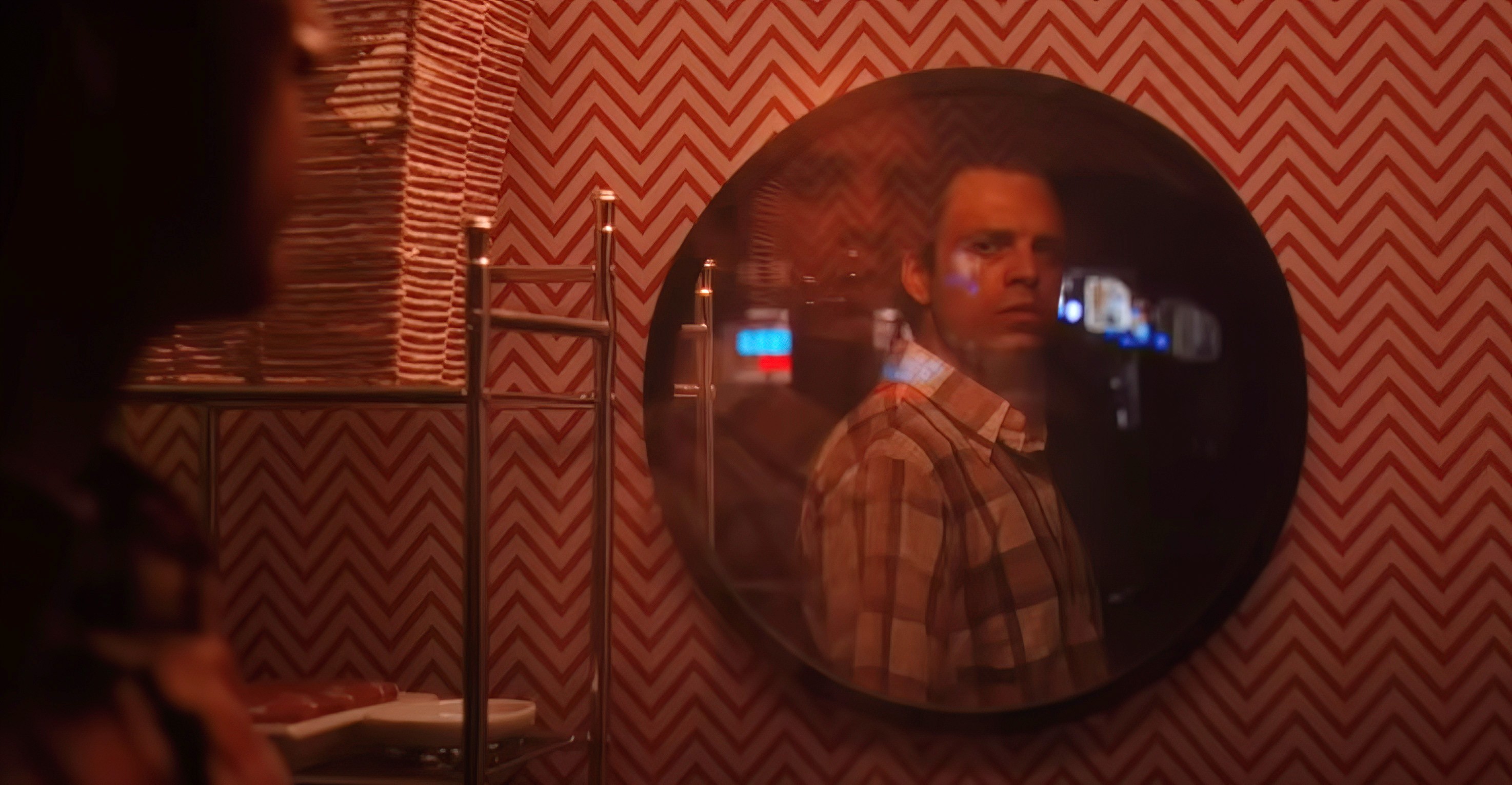 Edward (Sebastian Stan) looks at himself suspiciously in a round mirror in a dim red room in A Different Man