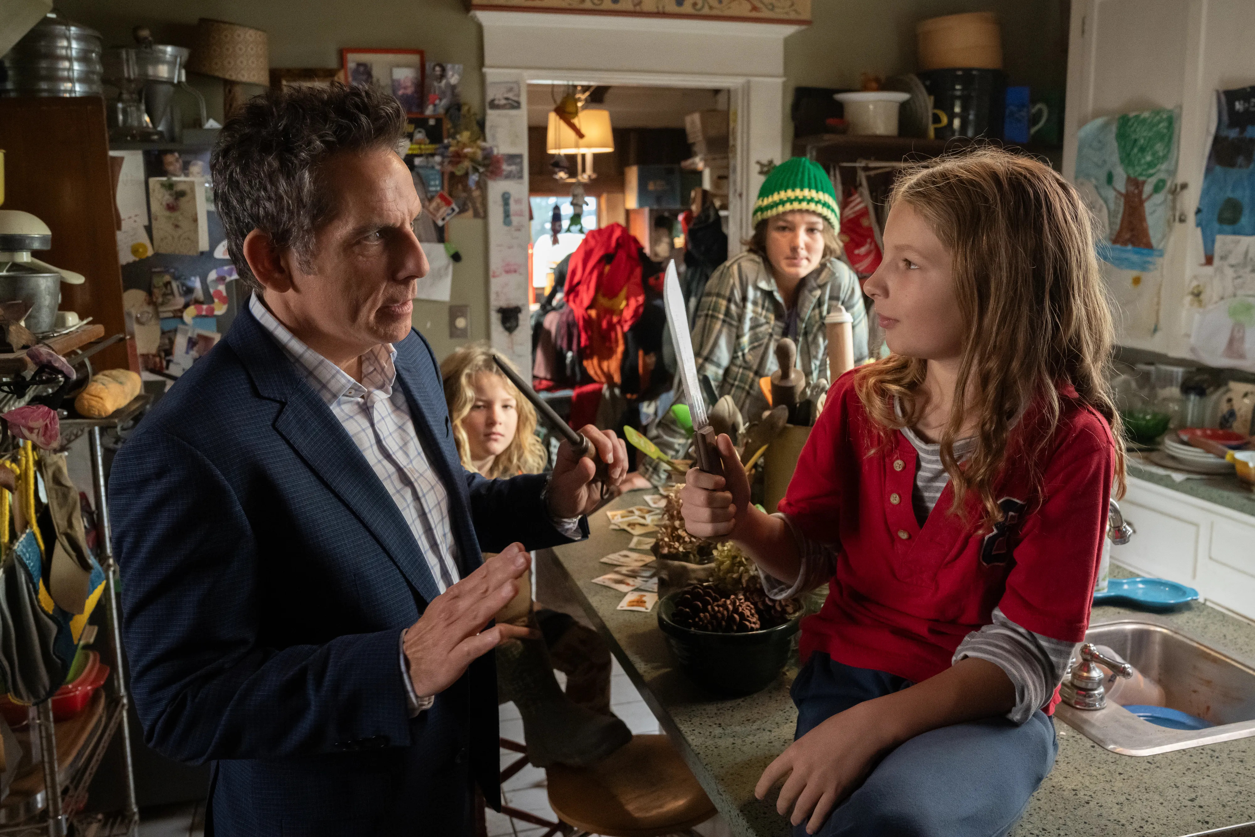 Ben Stiller standing in a crowded kitchen and staring at a young girl sitting on a counter with a knife in Nutcrackers.