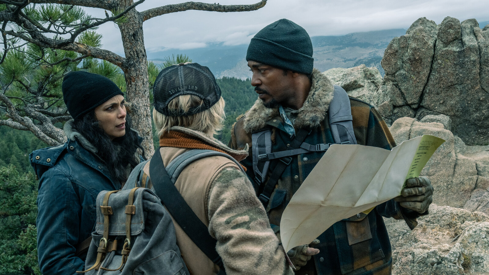 Morena Baccarin, Maddie Hasson, and Anthony Mackie standing in a wooded area next to rocky cliff holding a map in Elevation.