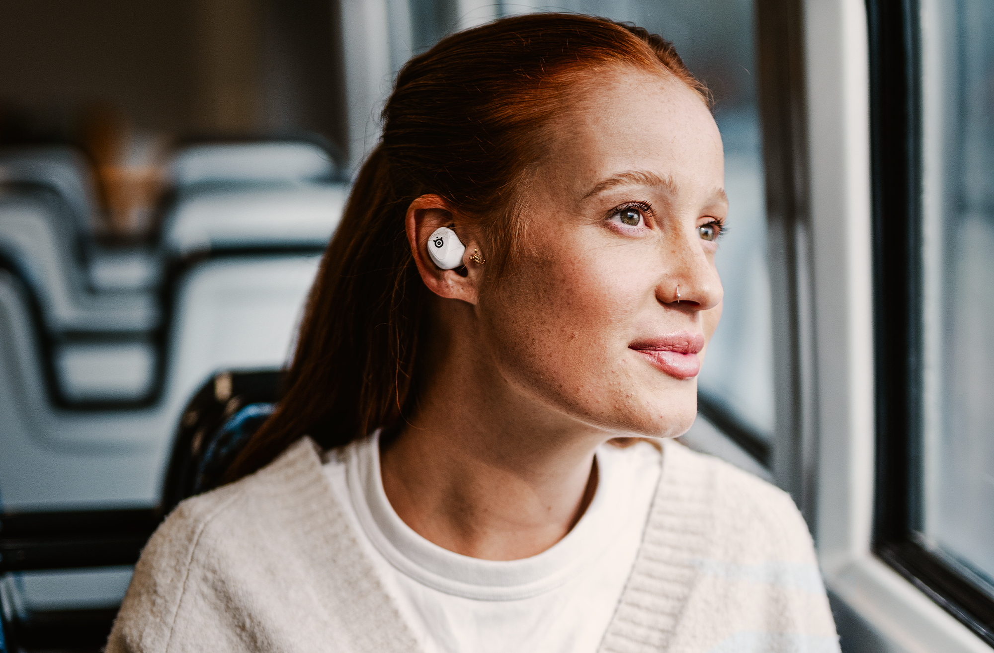 A stock photo of the white Steelseries GameBuds being worn by a woman with red hair