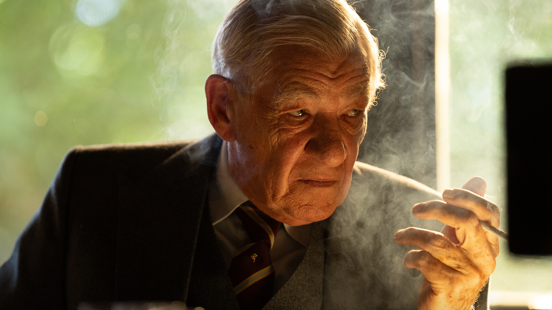 Ian McKellen scowling in a dark suit and holding a cigarette in The Critic.