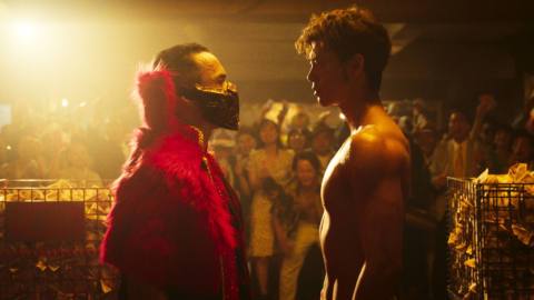 Kiryu (Ryoma Takeuchi) shirtless staring down a man dressed in a fluffy red getup with a mask