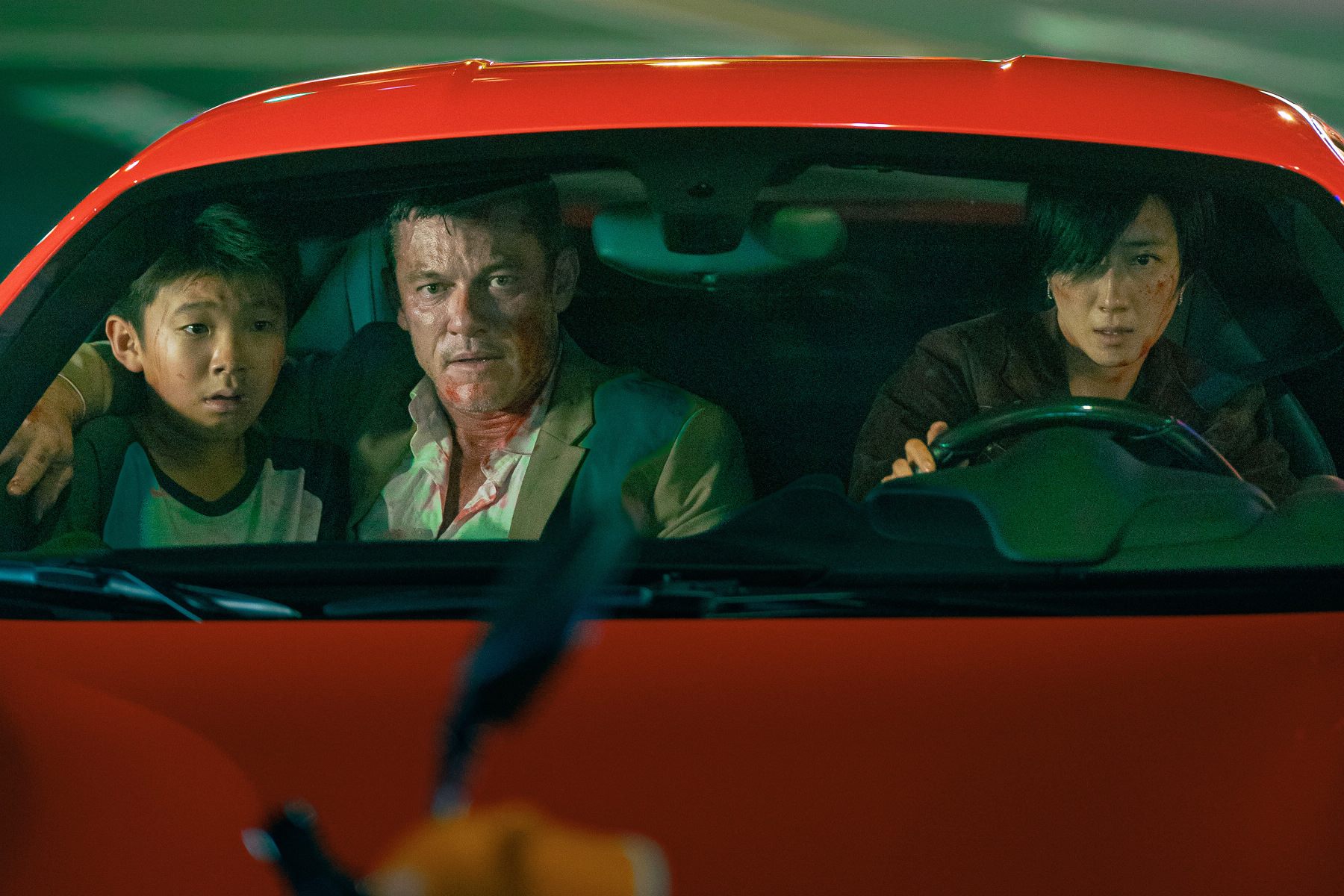 A man (Luke Evans) covered in a blood seated between a boy and a young woman driving a red car in Weekend in Taipei. A man (Luke Evans) covered in a blood seated between a boy and a young woman driving a red car in Weekend in Taipei.