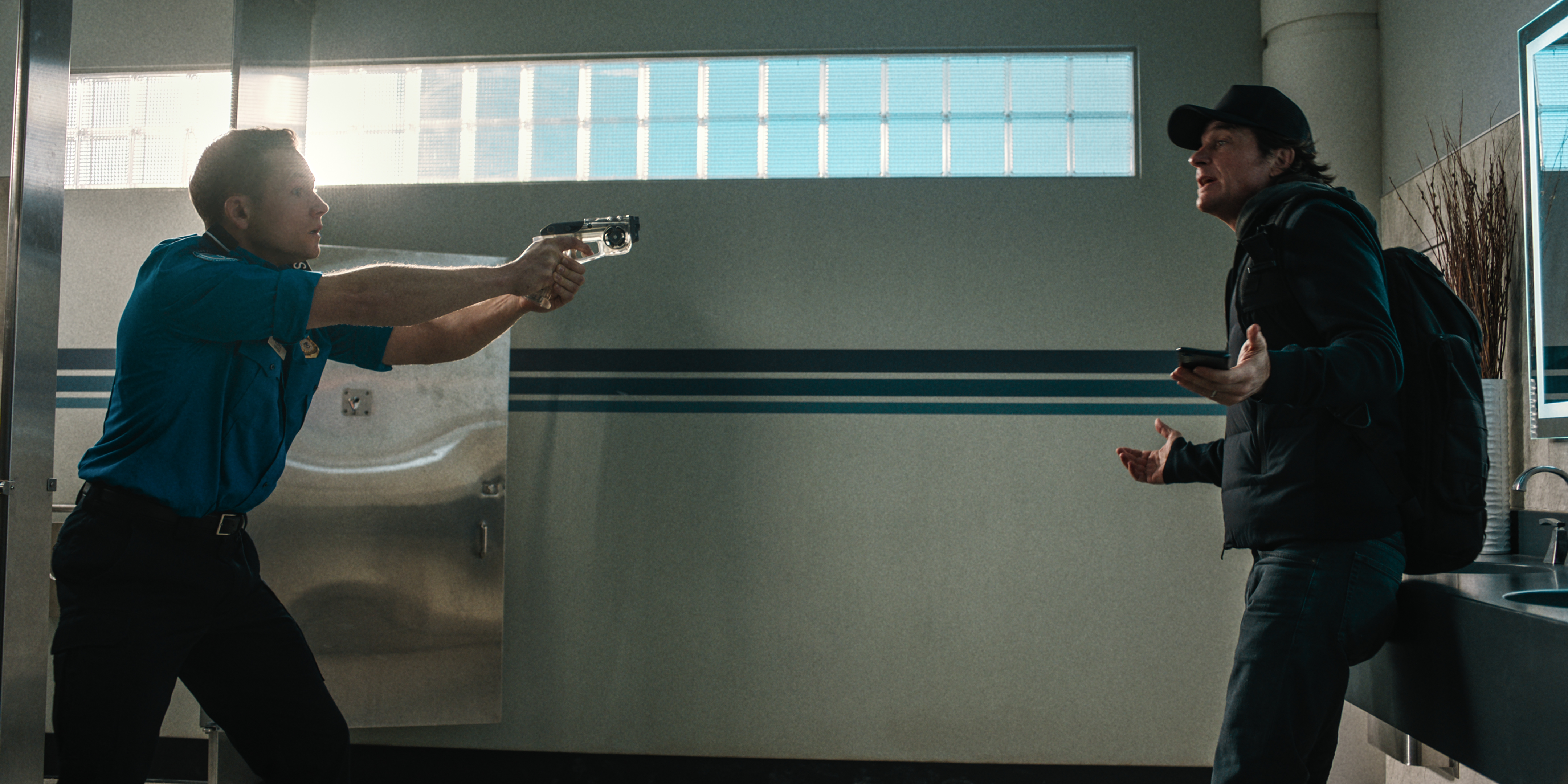Taron Egerton points a gun at Jason Bateman in an airport bathroom in Carry On Taron Egerton points a gun at Jason Bateman in an airport bathroom in Carry On