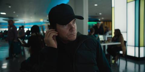 Jason Bateman in a black hat talking on the phone while walking through the airport in Carry-On