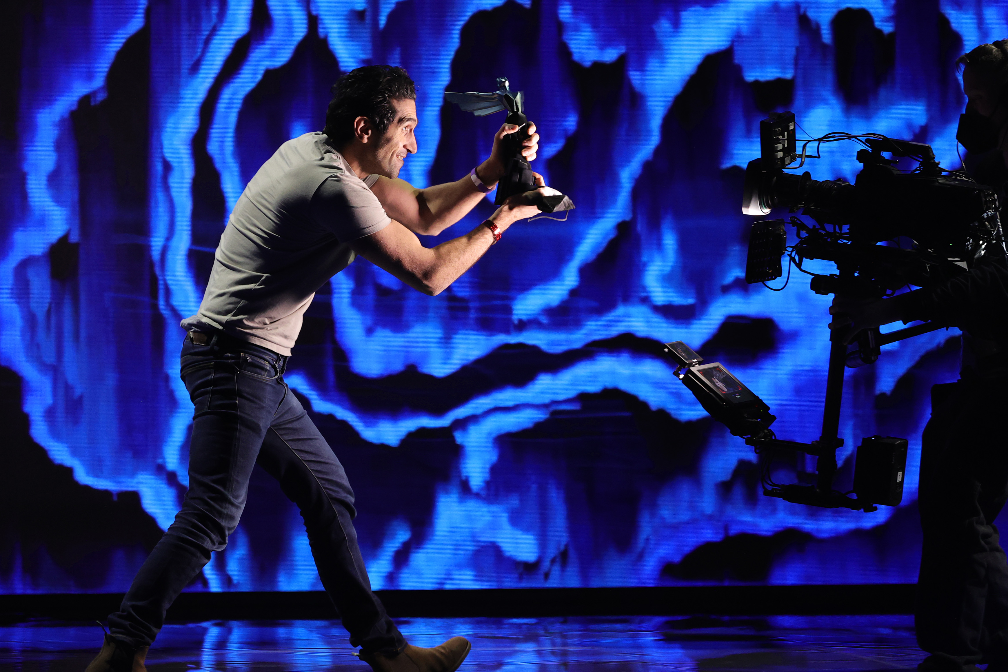 Josef Fares holds up a Game Awards statuette to a TV camera in front a blue background