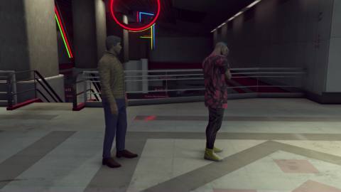 Two characters in GTA Online stand next to each other, one with his head in his hands. There are neon lights in the background