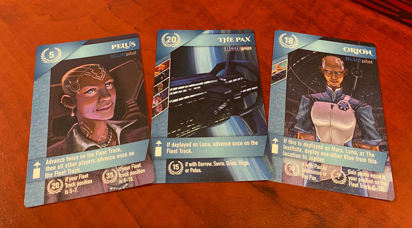 Three Blue cards from the Red Rising board game rest on a table. Three Blue cards from the Red Rising board game rest on a table.