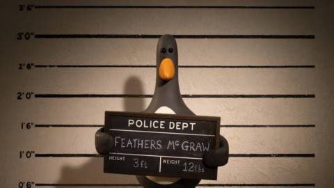 Feathers McGraw, a penguin with beady dark eyes, standing in front of a police lineup, holding a booking board in Wallace & Gromit: Vengeance Most Fowl