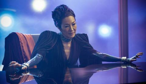 Michelle Yeoh as Georgiou in Star Trek: Section 31. She’s in a villainous dress with a fancy updo, sitting at a table and spreading her arms elegantly.