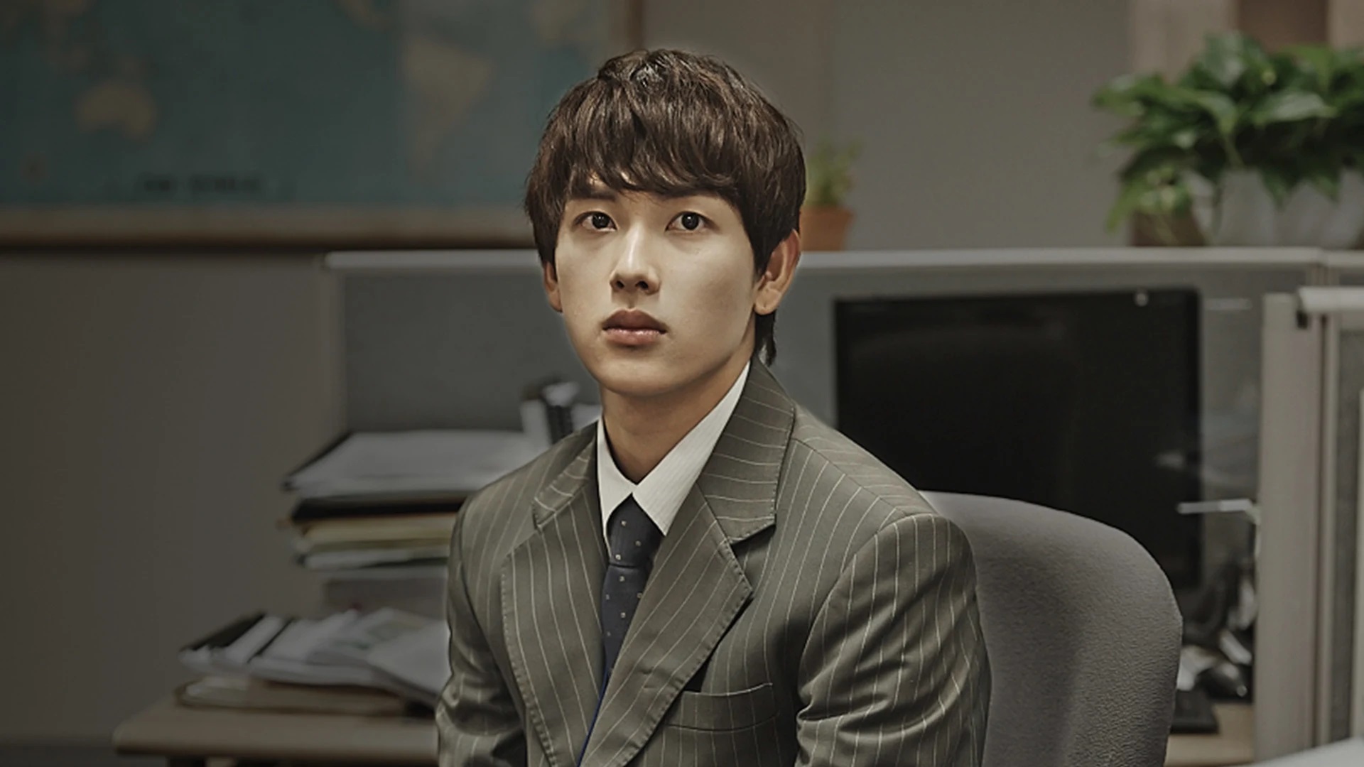 In Misaeng: Incomplete Life, a young man sits at a work station while wearing a suit.