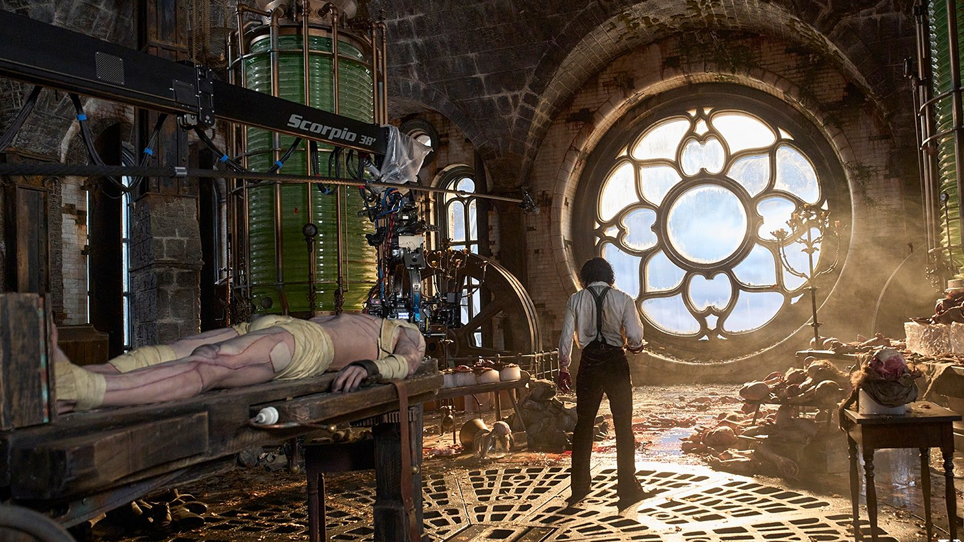 A behind the scenes shot of Victor Frankenstein (Oscar Isaac) standing beside the table of his creation (Jacob Elordi) in Frankenstein.