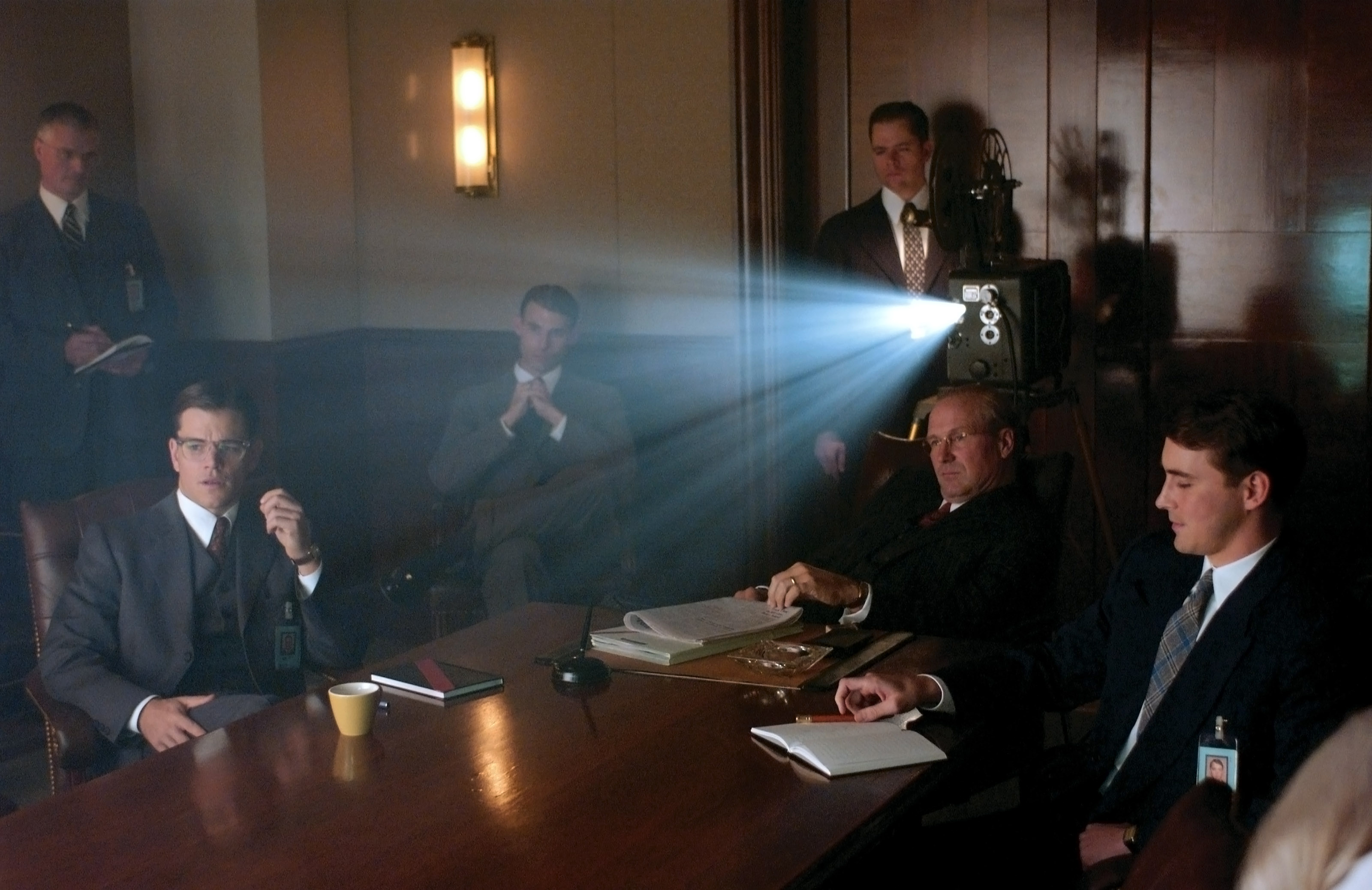 Matt Damon, John Hurt, and several other people sit around a table in suits watching something on a screen with a projector behind them in The Good Shepherd Matt Damon, John Hurt, and several other people sit around a table in suits watching something on a screen with a projector behind them in The Good Shepherd