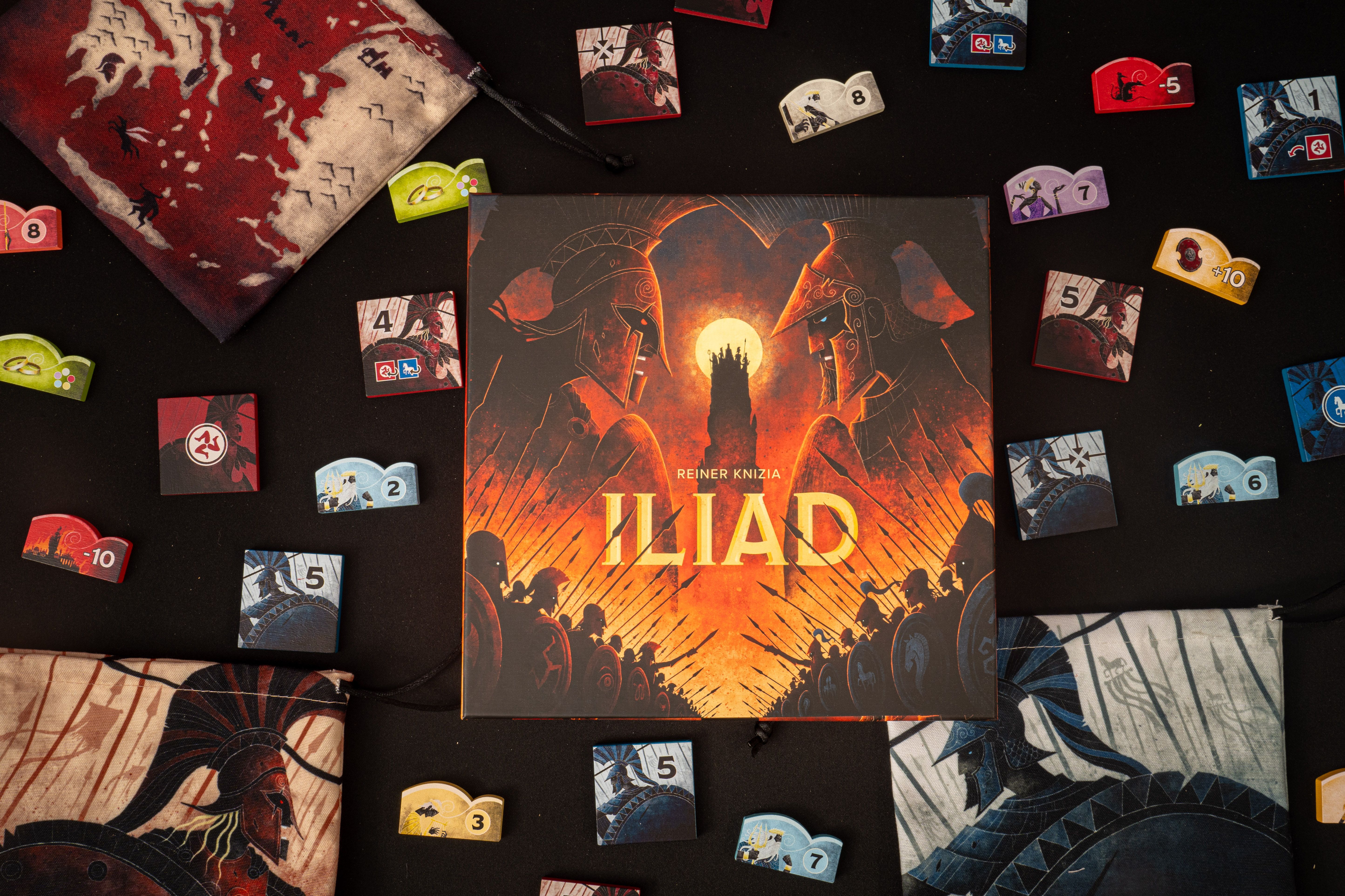 The box for Iliad sitting on a table surrounded by colorful tokens depicting gods and Greek warriors.