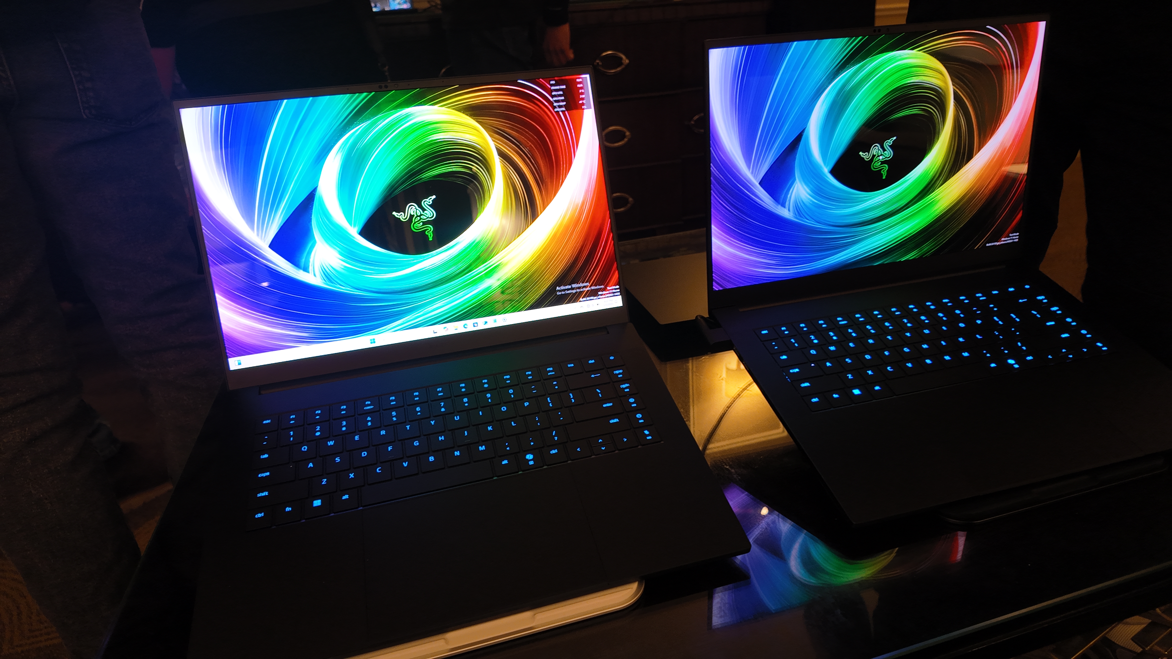 Two Razer Blade 16s side by side, glowing blue in a dark hotel suite.