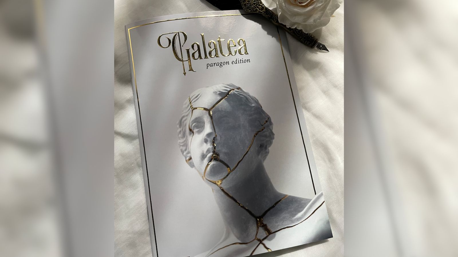 The Galatea physical book. The cover has a white marble statue with golden cracks and gold lettering for the title The Galatea physical book. The cover has a white marble statue with golden cracks and gold lettering for the title