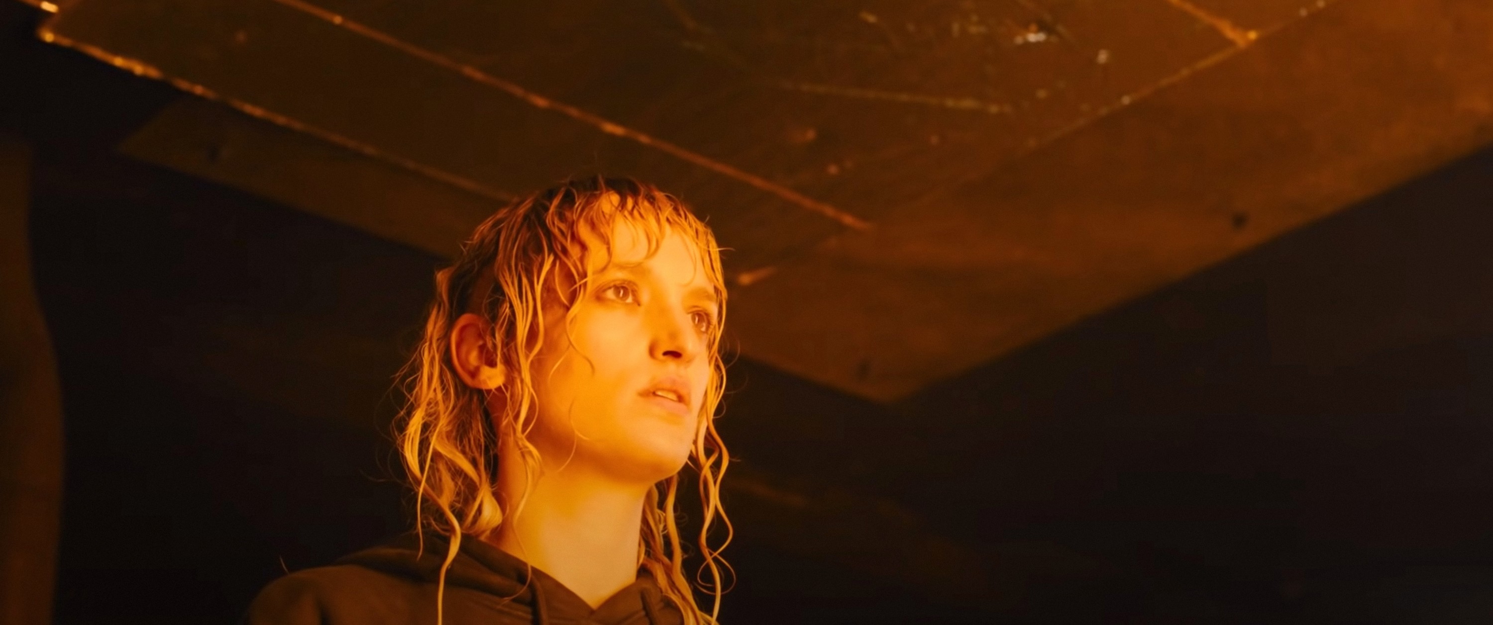 Alexia (Agathe Rousselle) standing and looking at something in awe in a still from Titane Alexia (Agathe Rousselle) standing and looking at something in awe in a still from Titane