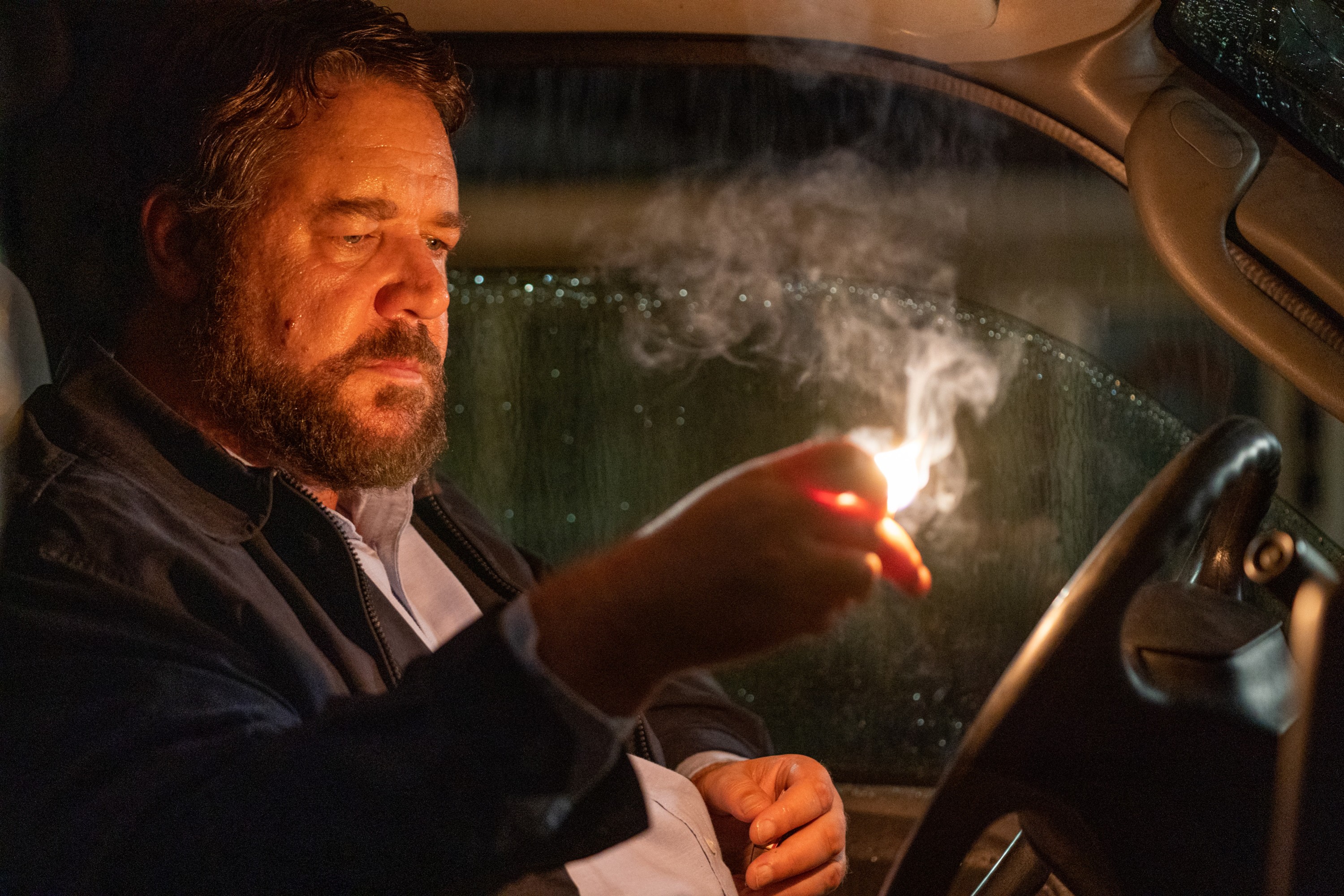 Russell Crowe sitting in the front of a pickup truck in Unhinged looking at a lit match in his hand Russell Crowe sitting in the front of a pickup truck in Unhinged looking at a lit match in his hand