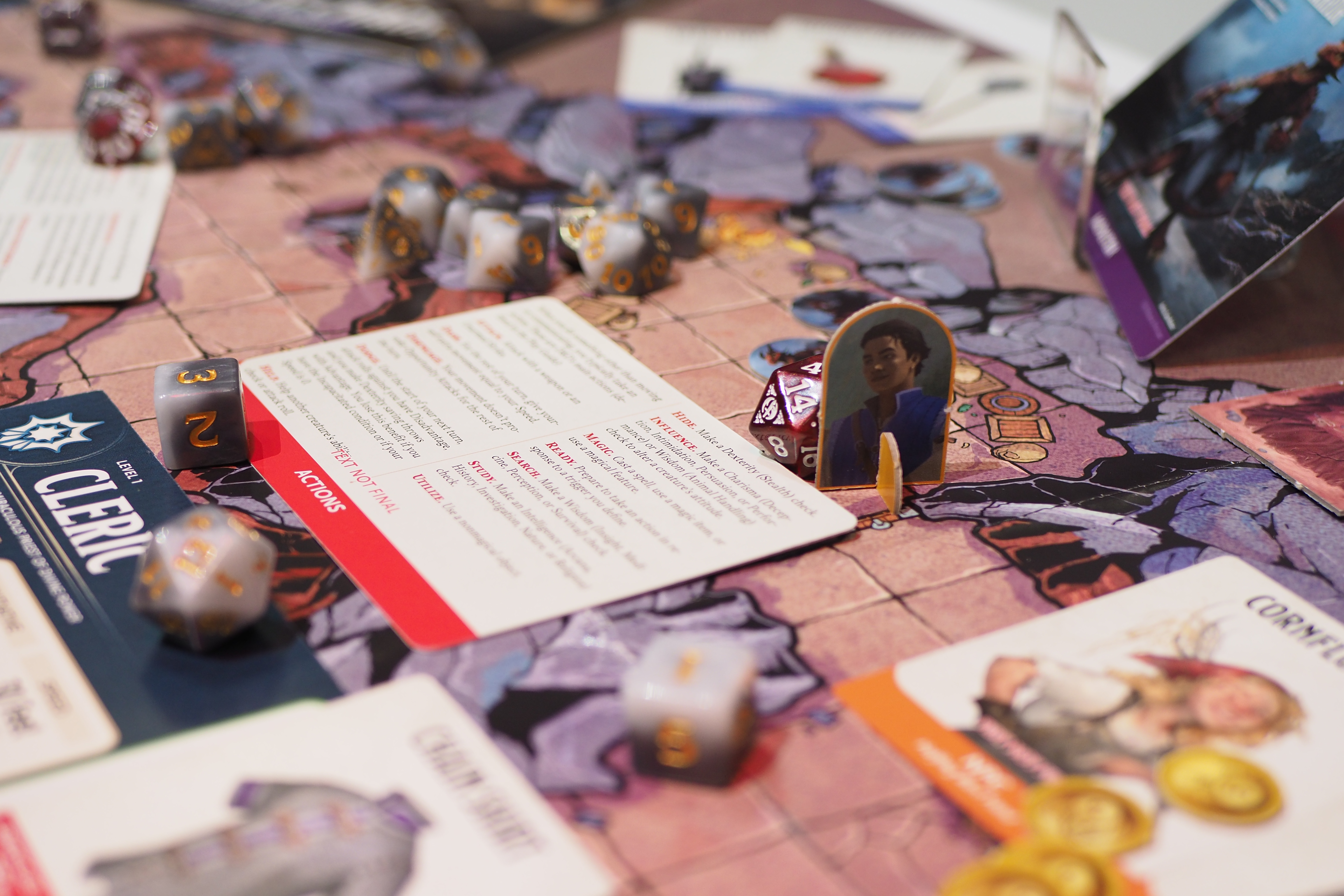 A side angle view of the Caves of Chaos adventure map included with the 2025 Dungeons & Dragons Starter Set. It shows multiple game pieces and a Cleric character sheet, including actions and dice.