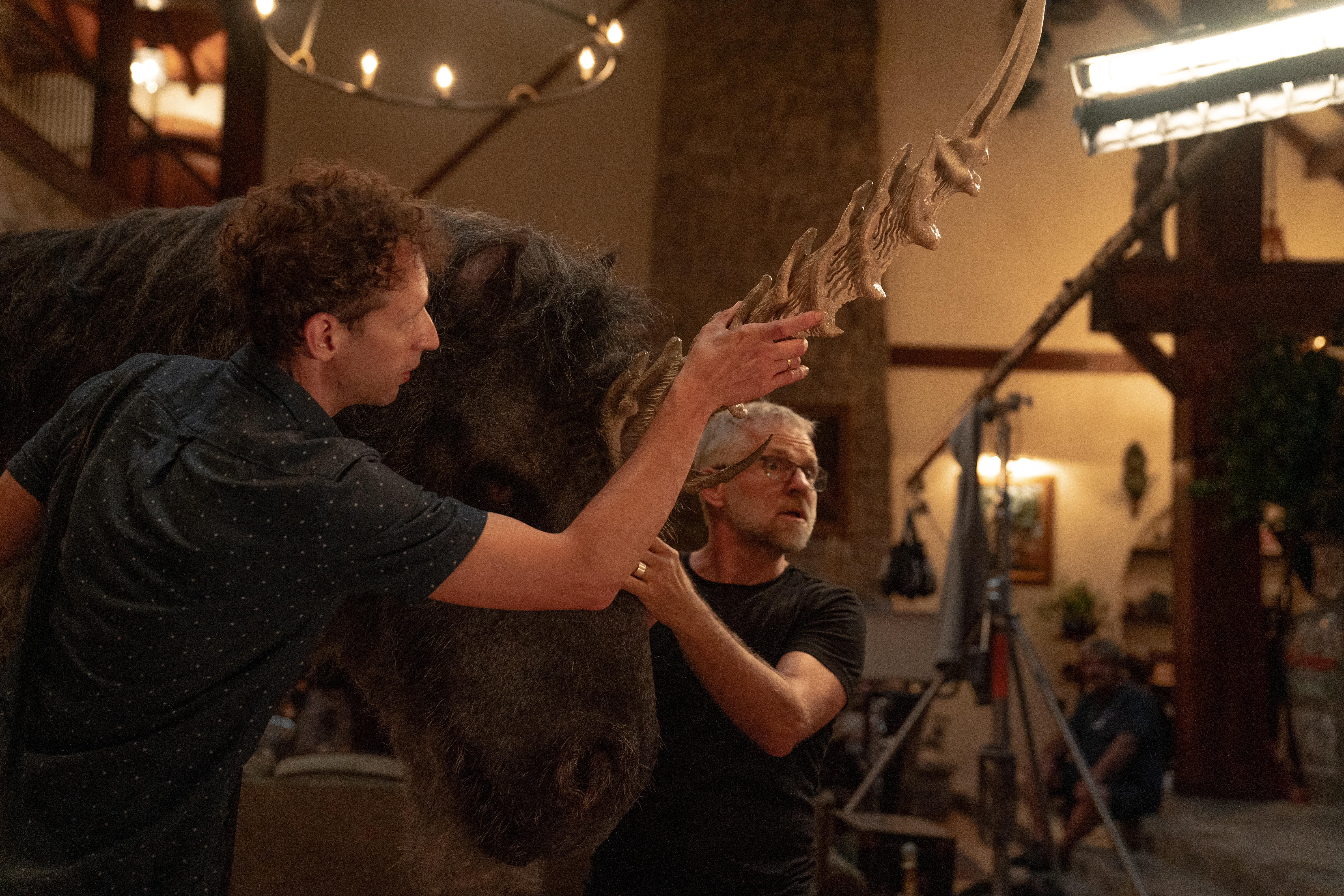 Alex Scharfman and crew adjust a prop unicorn head on the set of Death of a Unicorn. They’re inside a spacious mansion, with film equipment visible around them. The unicorn’s fur is purple-black, and its enormous horn is fearsomely ridged, with sharp, curving smaller spikes at its base. Alex Scharfman and crew adjust a prop unicorn head on the set of Death of a Unicorn. They’re inside a spacious mansion, with film equipment visible around them. The unicorn’s fur is purple-black, and its enormous horn is fearsomely ridged, with sharp, curving smaller spikes at its base.