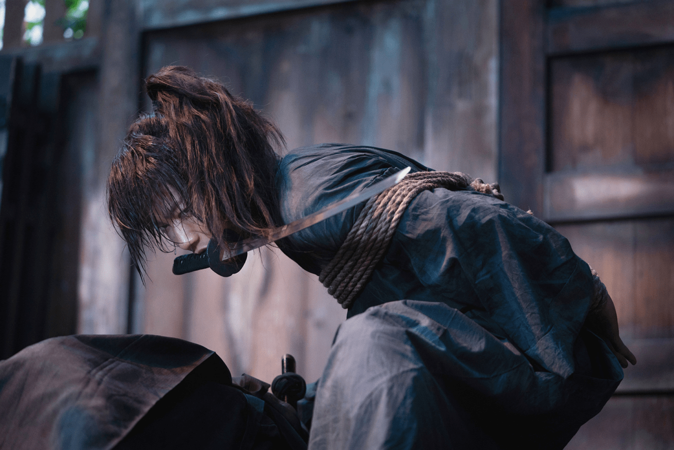 Takeru Satoh as Kenshin Himura holding a sword in his mouth with his hands tied behind his back in Rurouni Kenshin: The Beginning. Takeru Satoh as Kenshin Himura holding a sword in his mouth with his hands tied behind his back in Rurouni Kenshin: The Beginning.