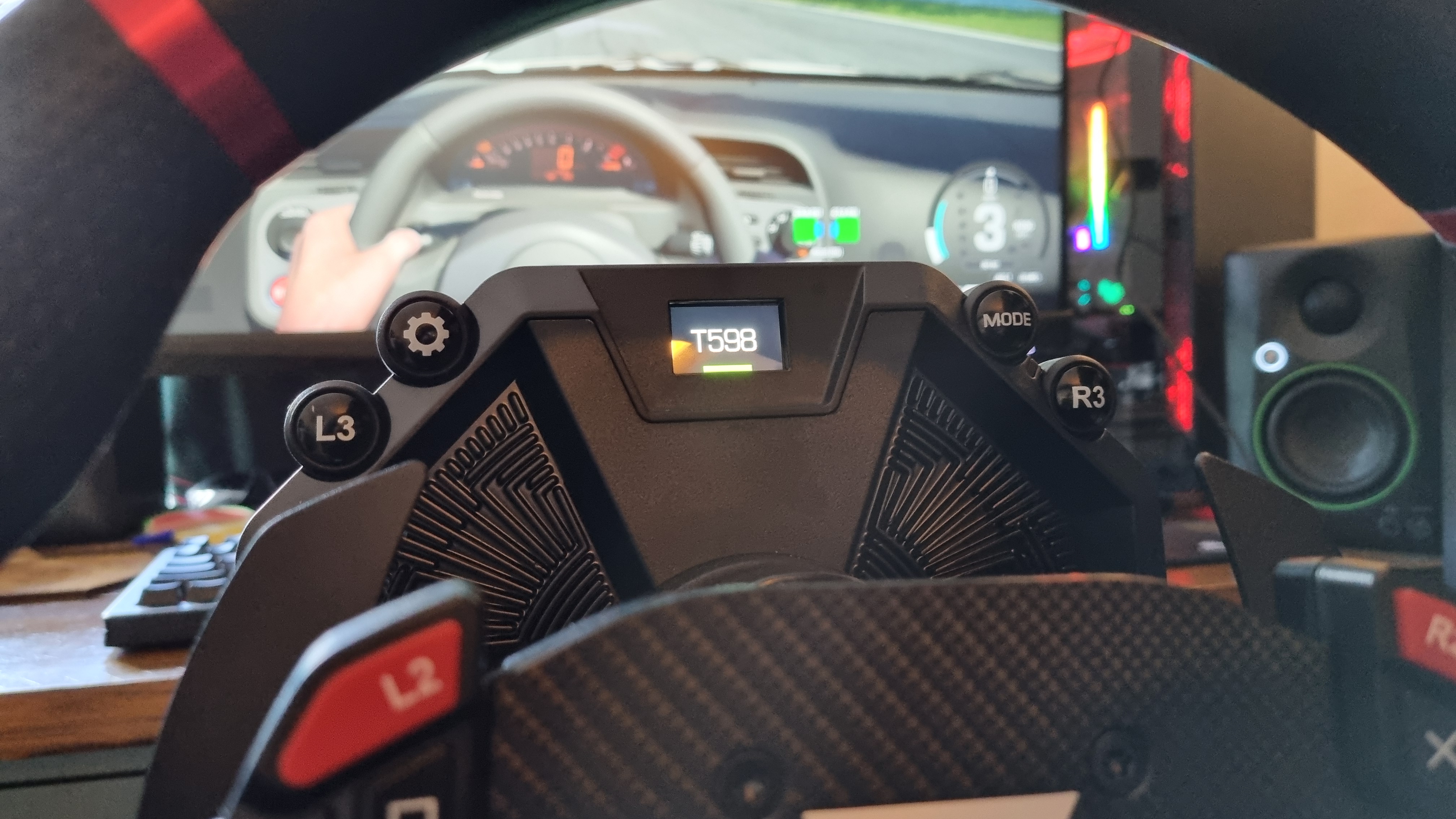 The wheelbase screen of the Thrustmaster T598, with Assetto Corsa Evo in the background