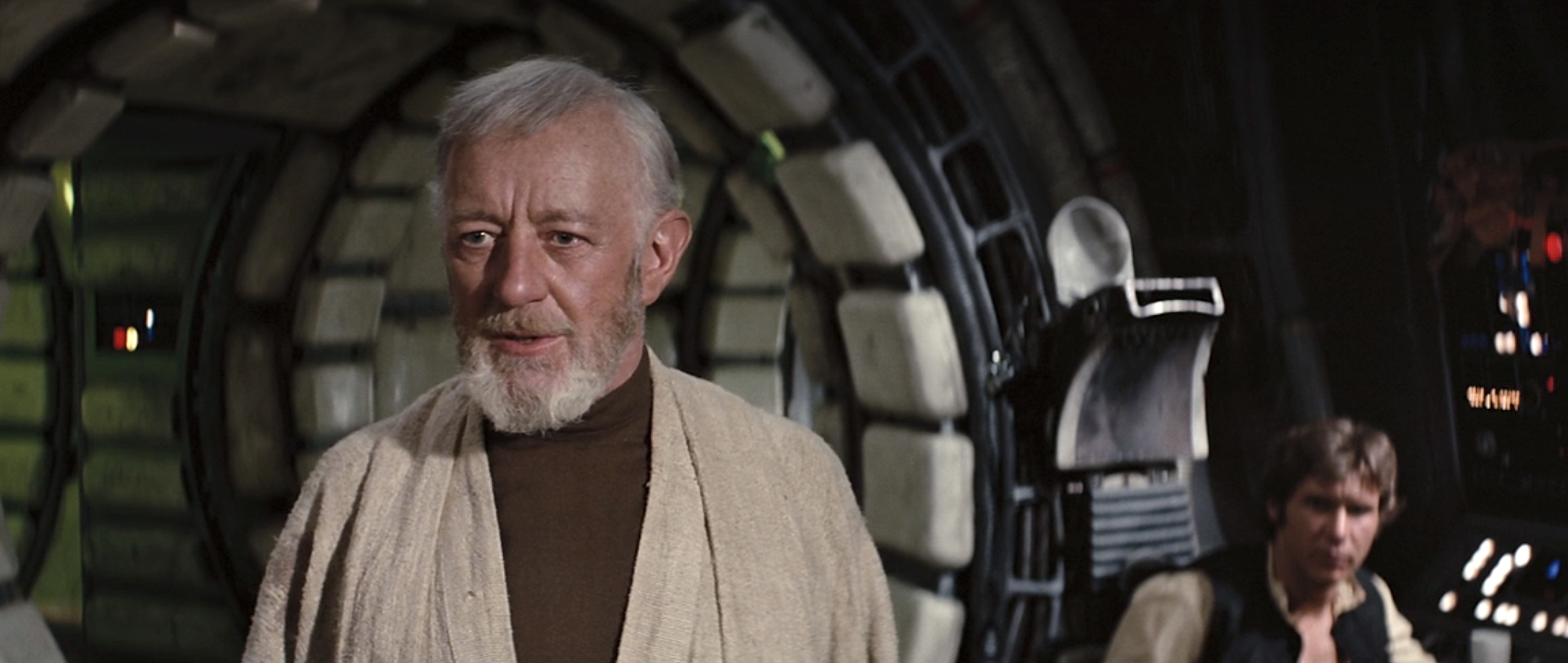 Alec Guinness as Obi-Wan Kenobi, standing in the Millennium Falcon with Han Solo (Harrison Ford) seated at a console in the background in Star Wars: Episode IV – A New Hope Alec Guinness as Obi-Wan Kenobi, standing in the Millennium Falcon with Han Solo (Harrison Ford) seated at a console in the background in Star Wars: Episode IV – A New Hope