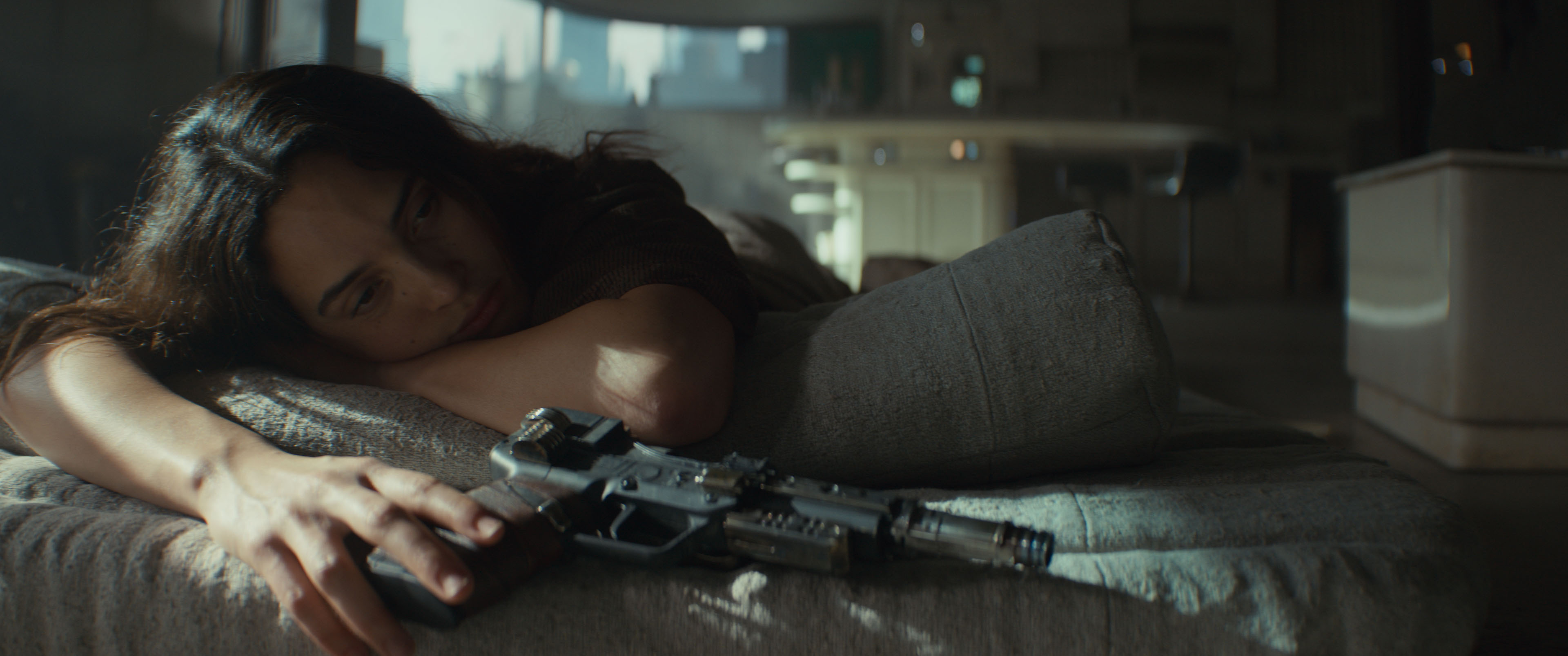 Bix Caleen (Adria Arjona) lies wearily on a bed in a dark room, fingers resting on the butt of a blaster, in Andor season 2